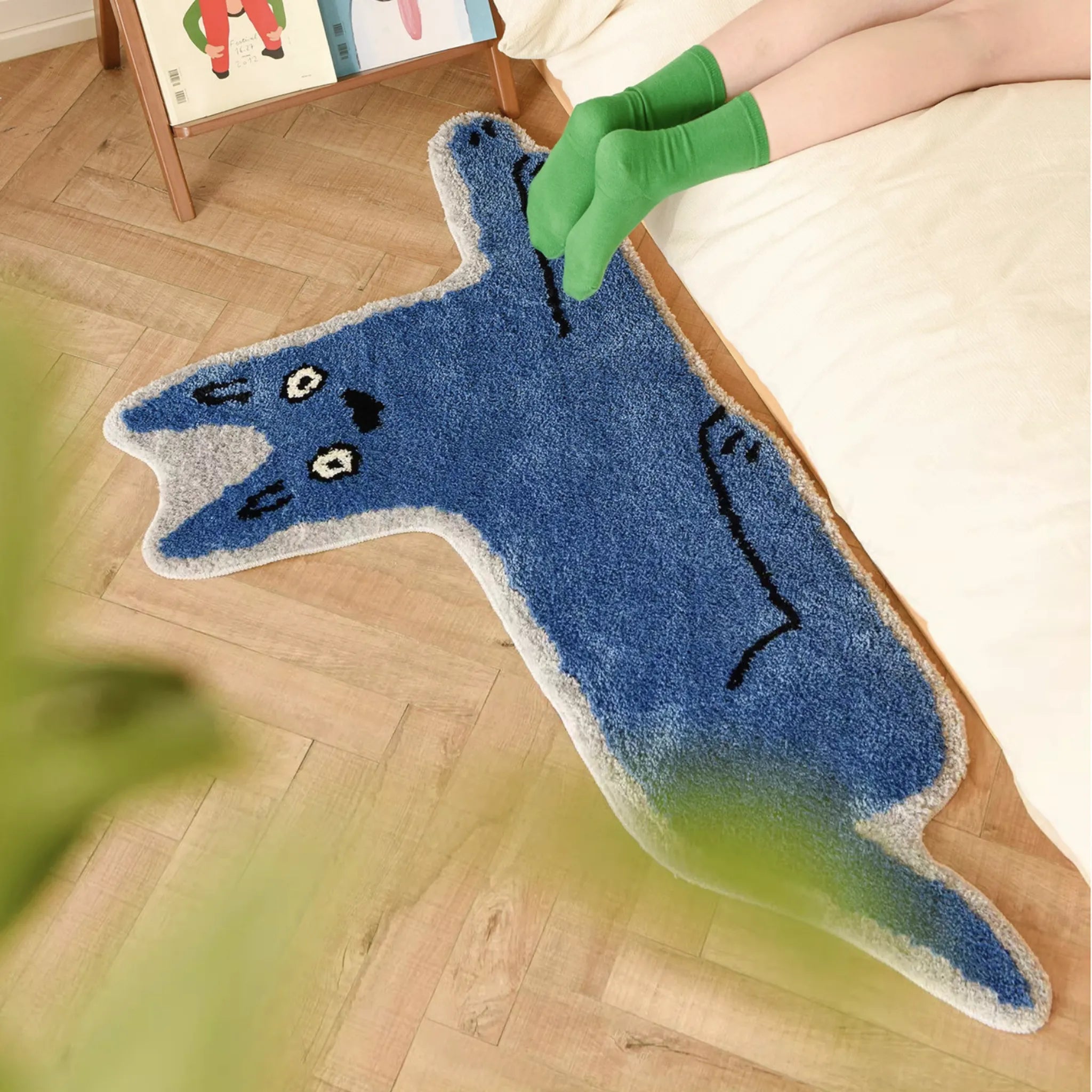 Goofy Wide Eyed Blue Cat Shaped Tufted Rug on a wooden floor with a person wearing green socks.