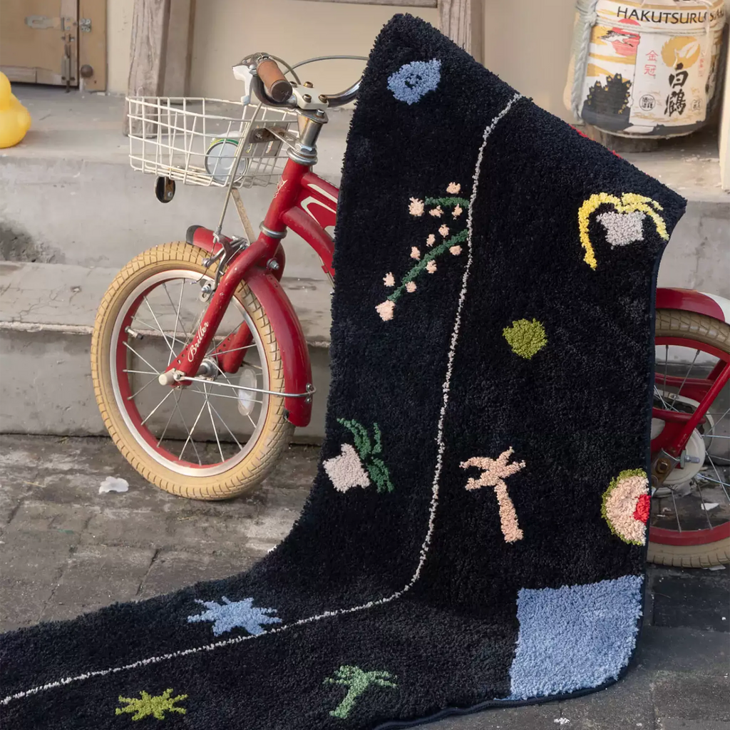 Black graphic motif sock shaped tufted rug with raised flower moon palm and starburst details styled beside a red bicycle by Housenfriends