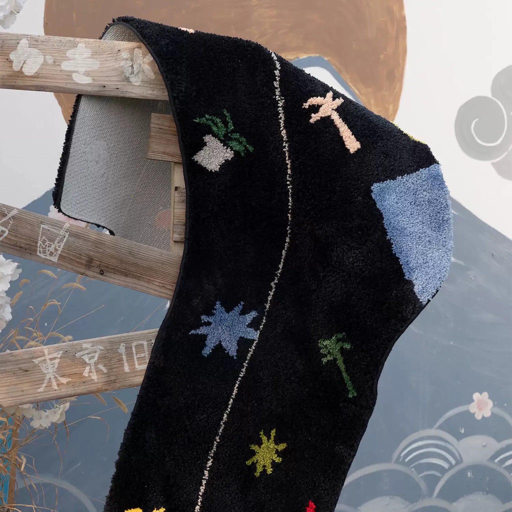 Black oversized sock shaped tufted rug with pale blue heel patch, palm motifs and blue starburst hanging on a wooden ladder by Housenfriends