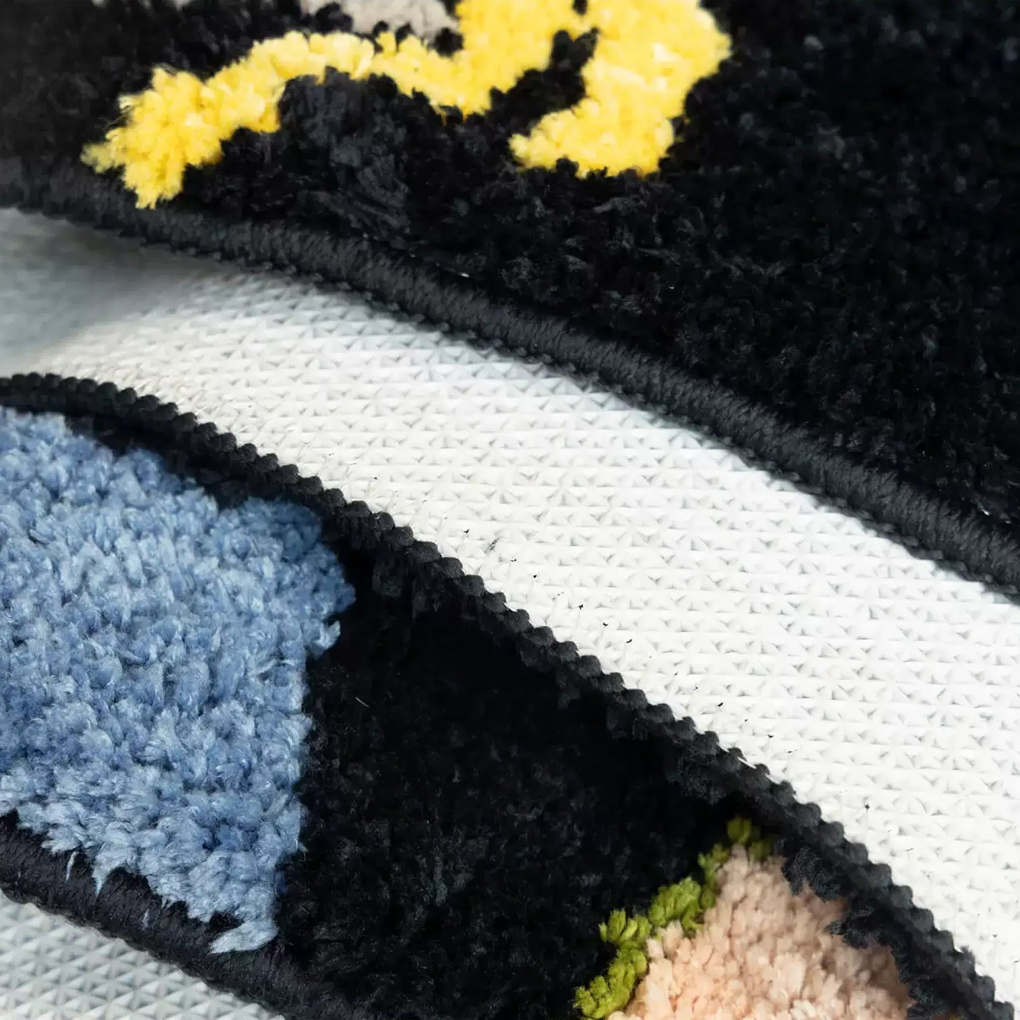 Close up of black graphic sock shaped tufted rug showing pale blue heel patch, yellow motif and non-slip backing by Housenfriends