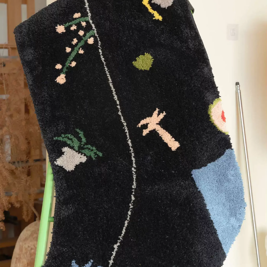 Black graphic motif sock shaped rug close up with raised flower sprig, palm tree and pale blue heel patch by Housenfriends