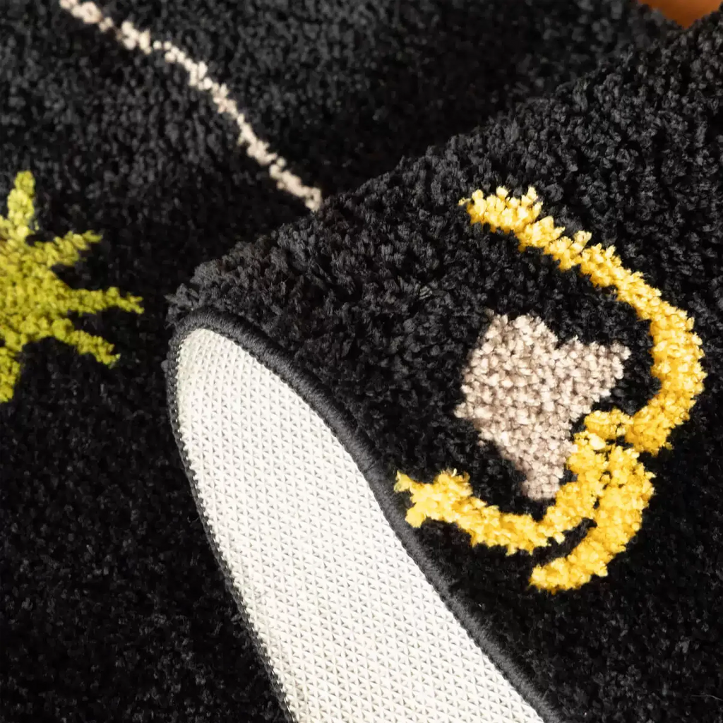 Close up of black sock shaped tufted rug showing raised yellow moon motif, soft black pile and non-slip backing by Housenfriends