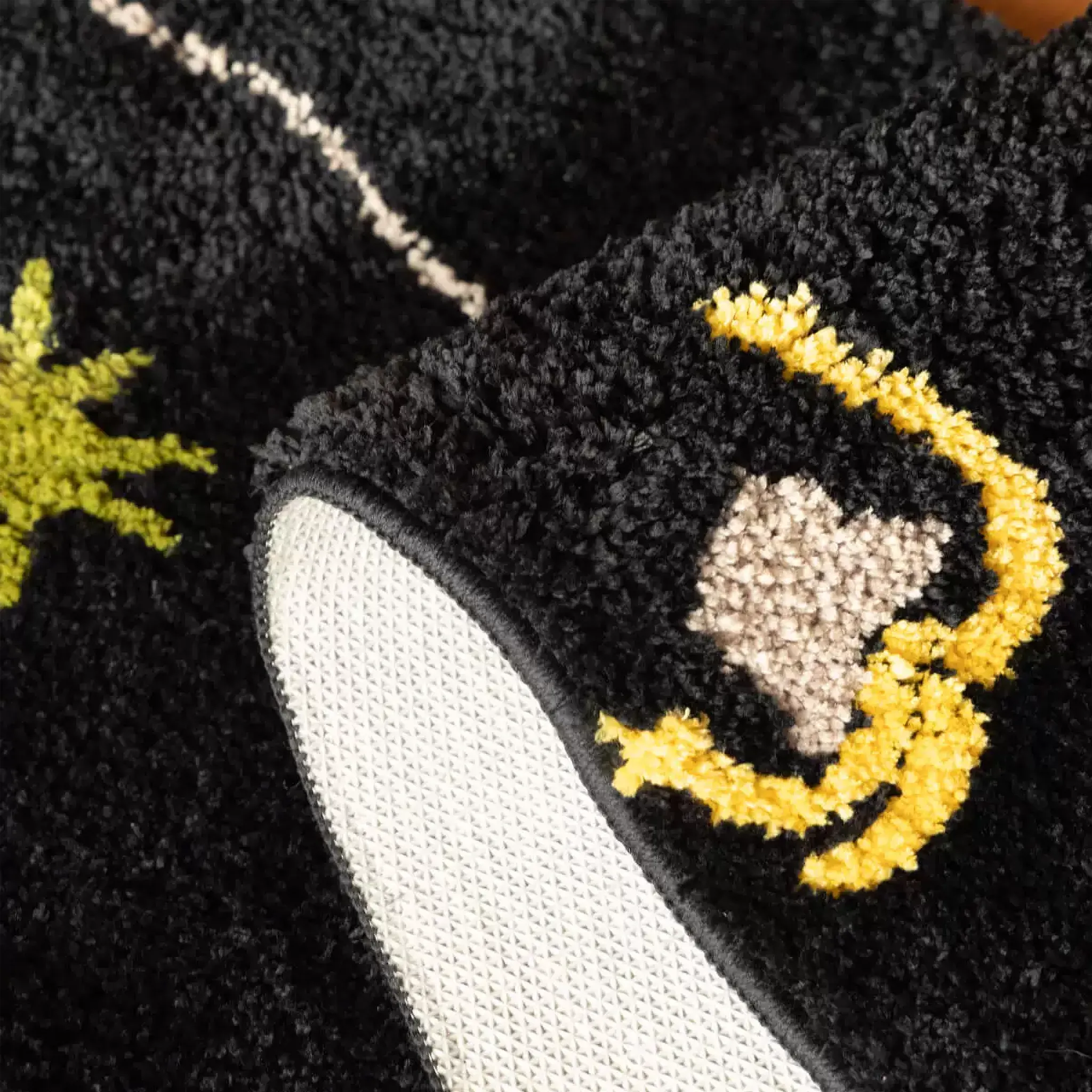 Close up of black sock shaped tufted rug showing raised yellow moon motif, soft black pile and non-slip backing by Housenfriends