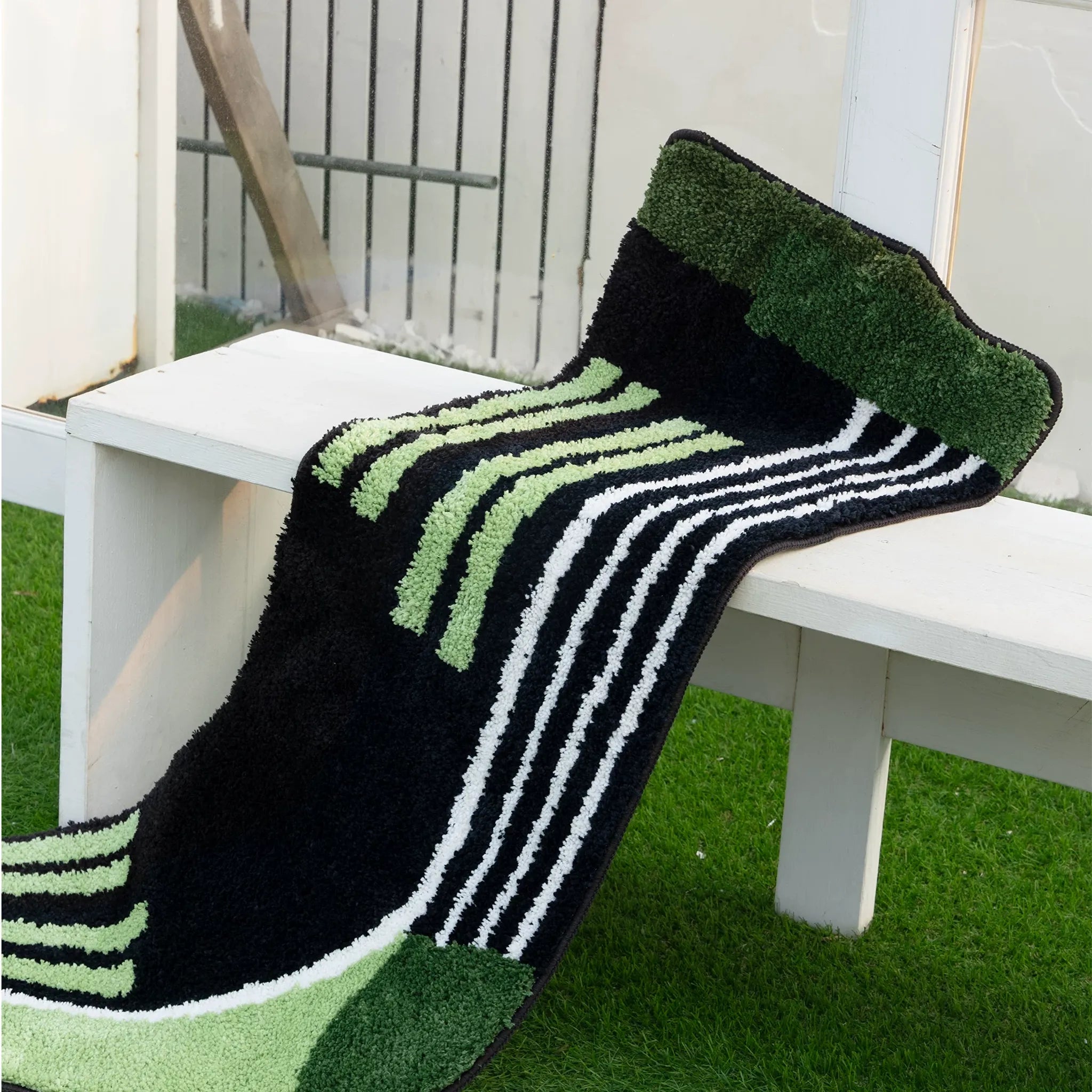Black and green graphic striped sock shaped tufted rug styled over a white bench by Housenfriends
