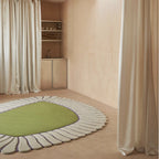 Coquille Green Seashell Shaped Sculpted Rug on a beige floor in a room with curtains and shelves.
