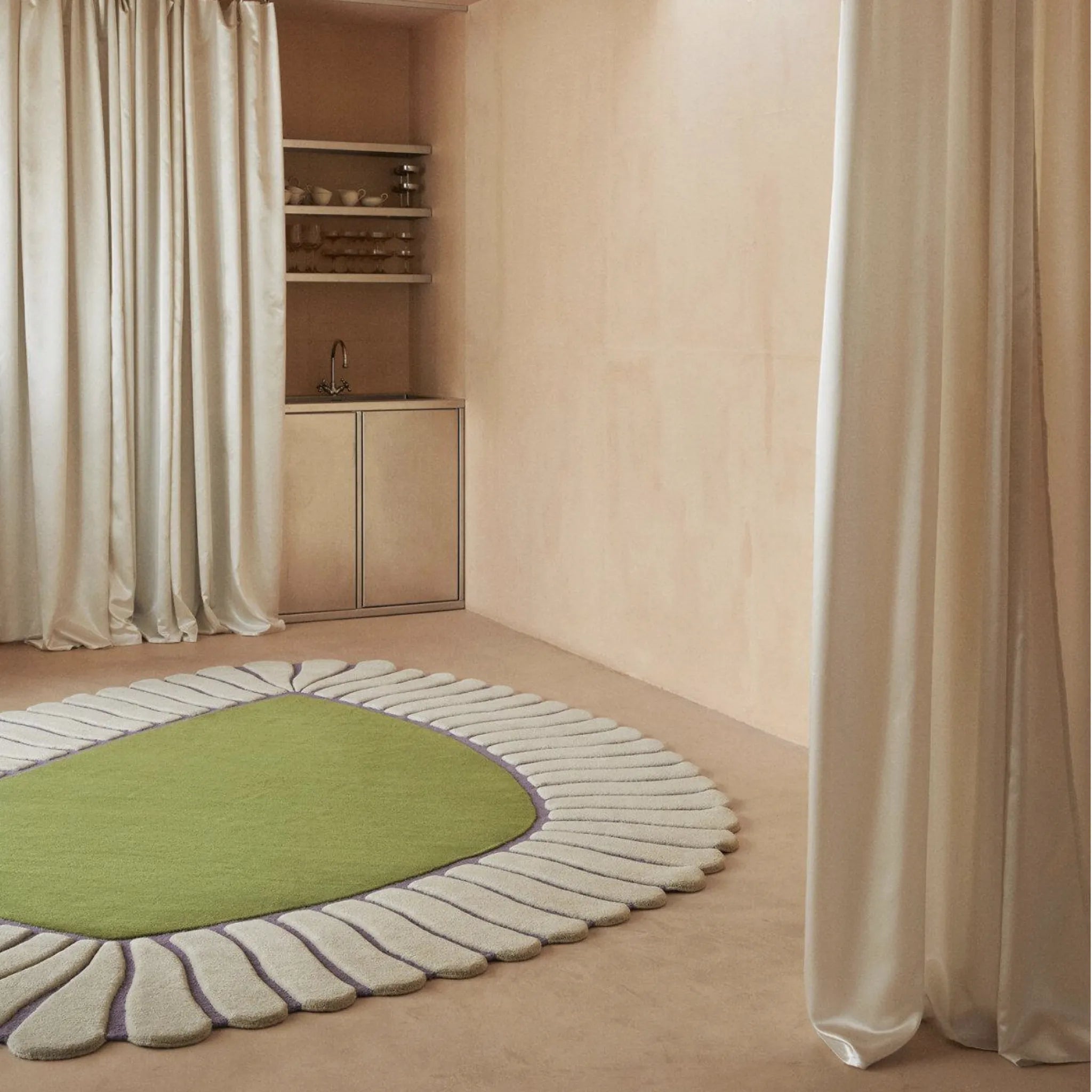 Coquille Green Seashell Shaped Sculpted Rug on a beige floor in a room with curtains and shelves.