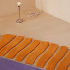 Coquille Purple Orange Seashell Shaped Sculpted Rug by Housenfriends on a beige floor with a small lamp.