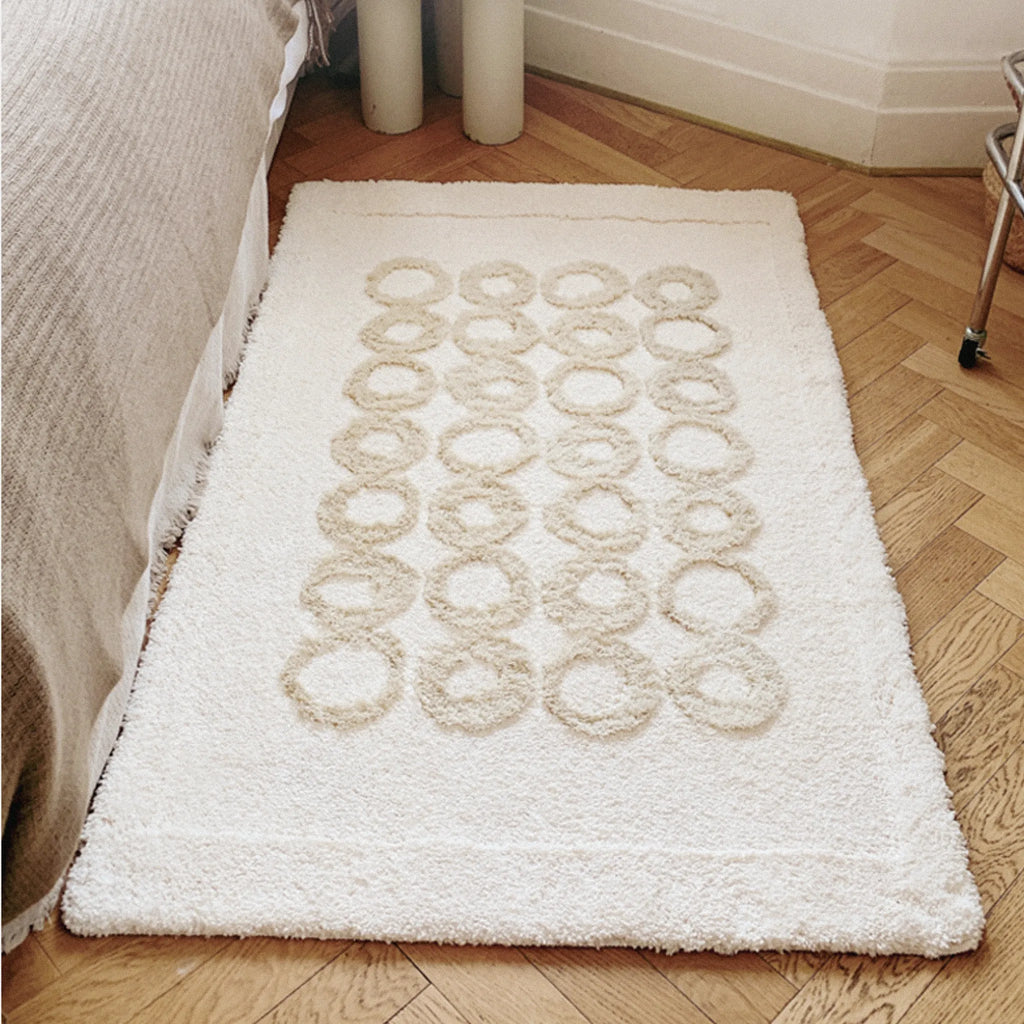 Nola Cream Beige Sculpted Circle High Low Tufted Rug placed by a bedside on a wooden floor.