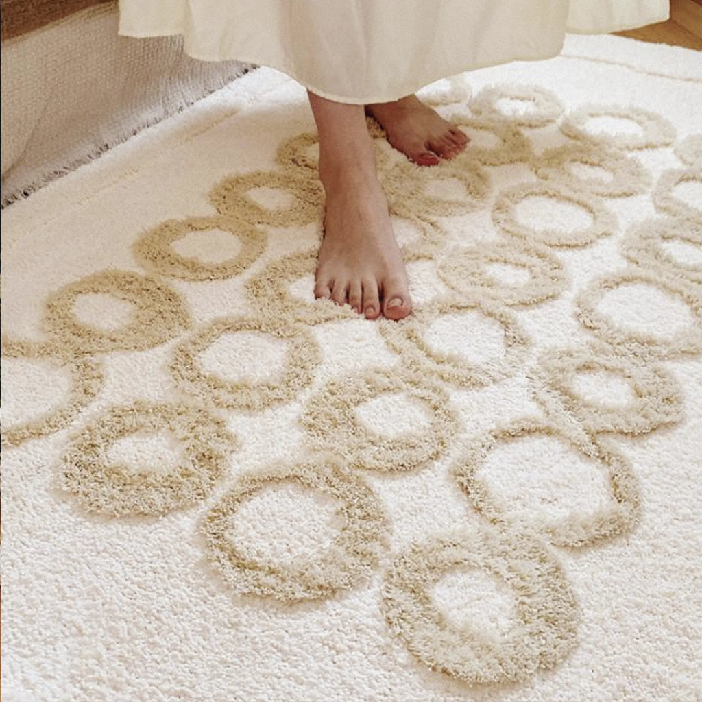 Close-up of a cream tufted rug with beige circular designs, showing feet stepping onto it.