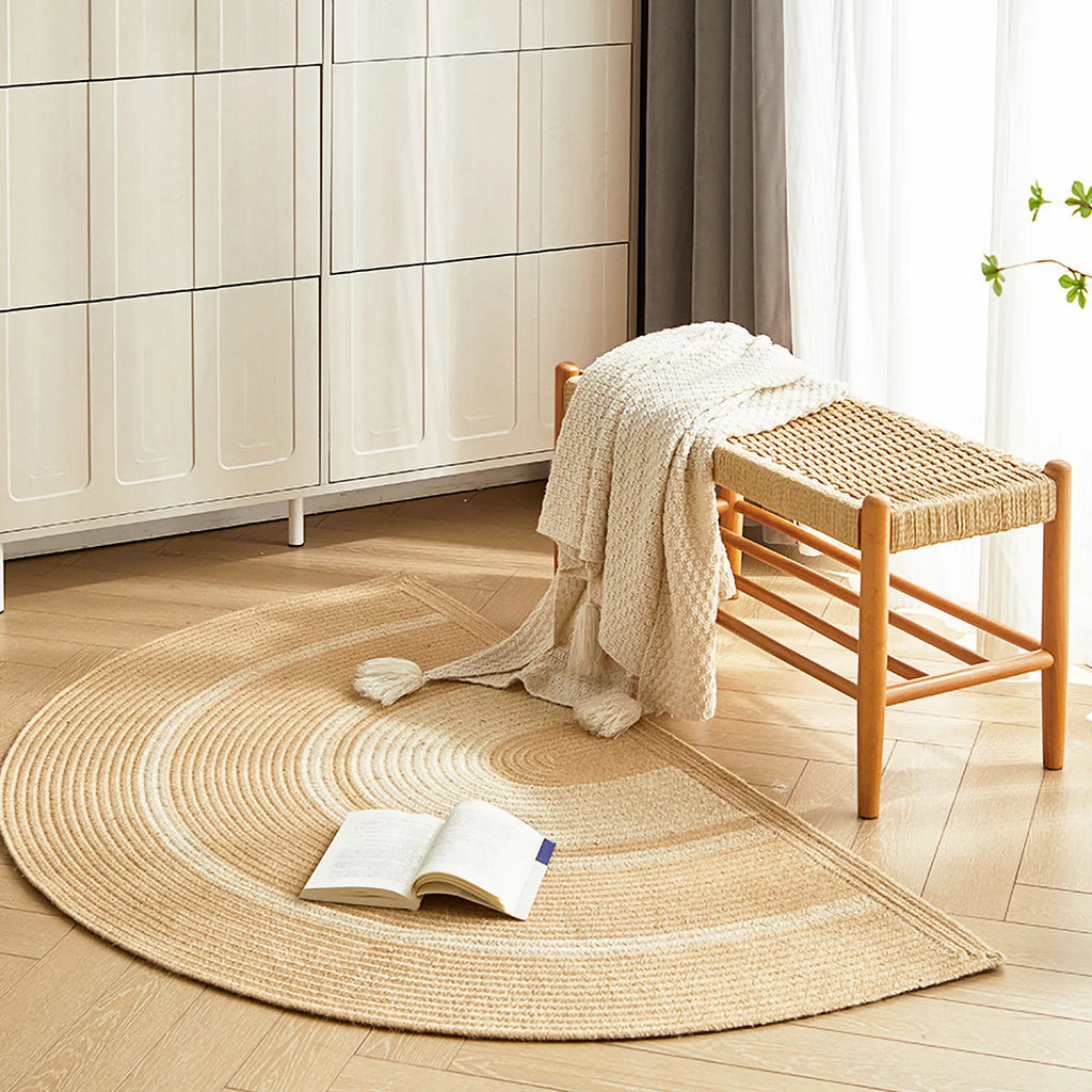 Elina Beige & Natural Jute-Blend Braided Half Moon Rug on a wooden floor with a stool and book in a room.