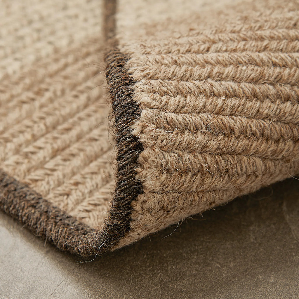 Close-up of a textured Elina Brown & Beige Wool-Blend Braided Half Moon Rug corner on a neutral background