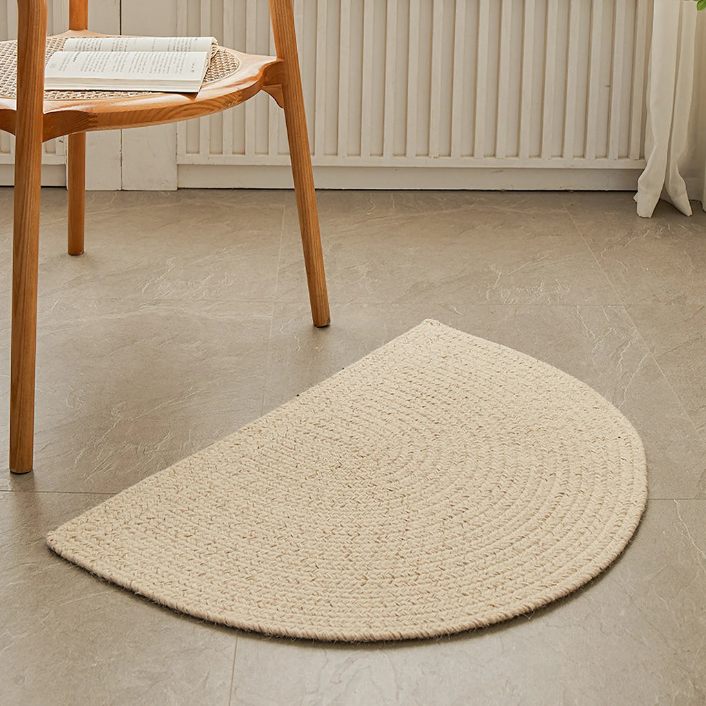 Elina Cream Wool-Blend Braided Half Moon Rug rug on a tiled floor with a wooden chair in the background.