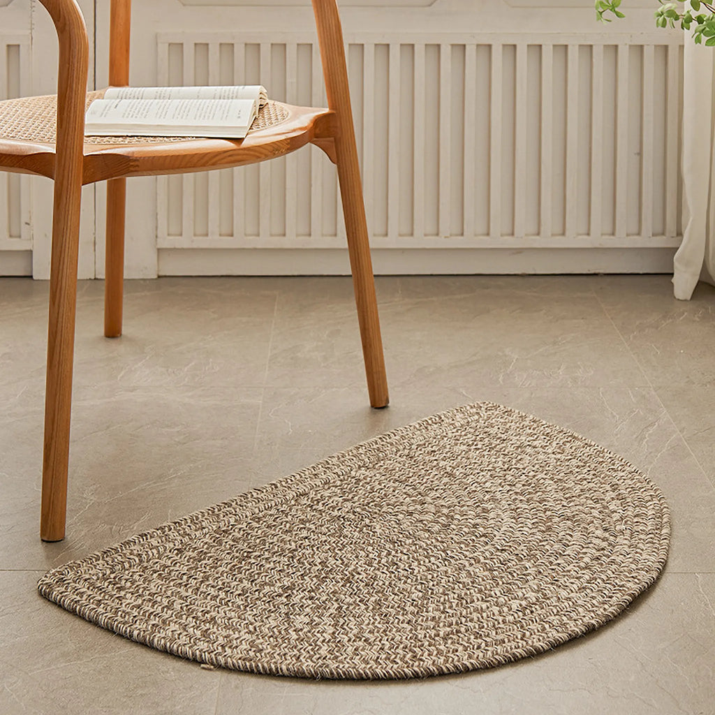 Elina Warm Beige Wool-Blend Braided Half Moon Rug on a stone floor with a wooden chair in the background.