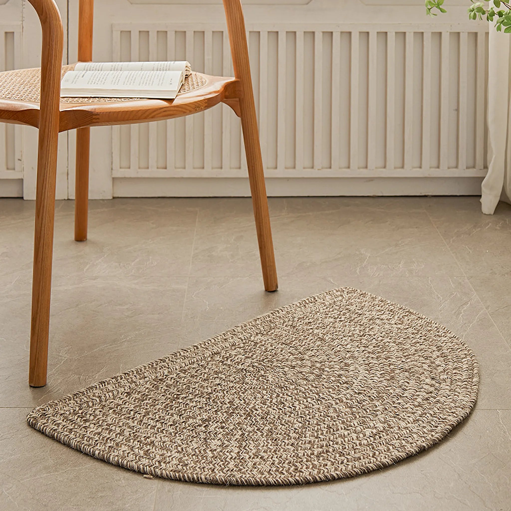 Elina Warm Beige Wool-Blend Braided Half Moon Rug on a stone floor with a wooden chair in the background.