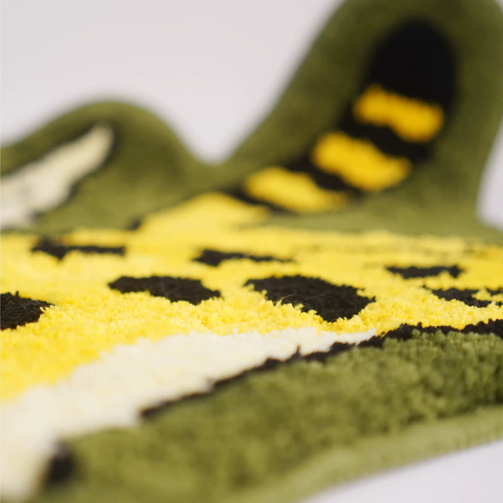 Close up of soft tufted leopard rug texture with yellow pile, black spots, cream wing detail and olive green edge