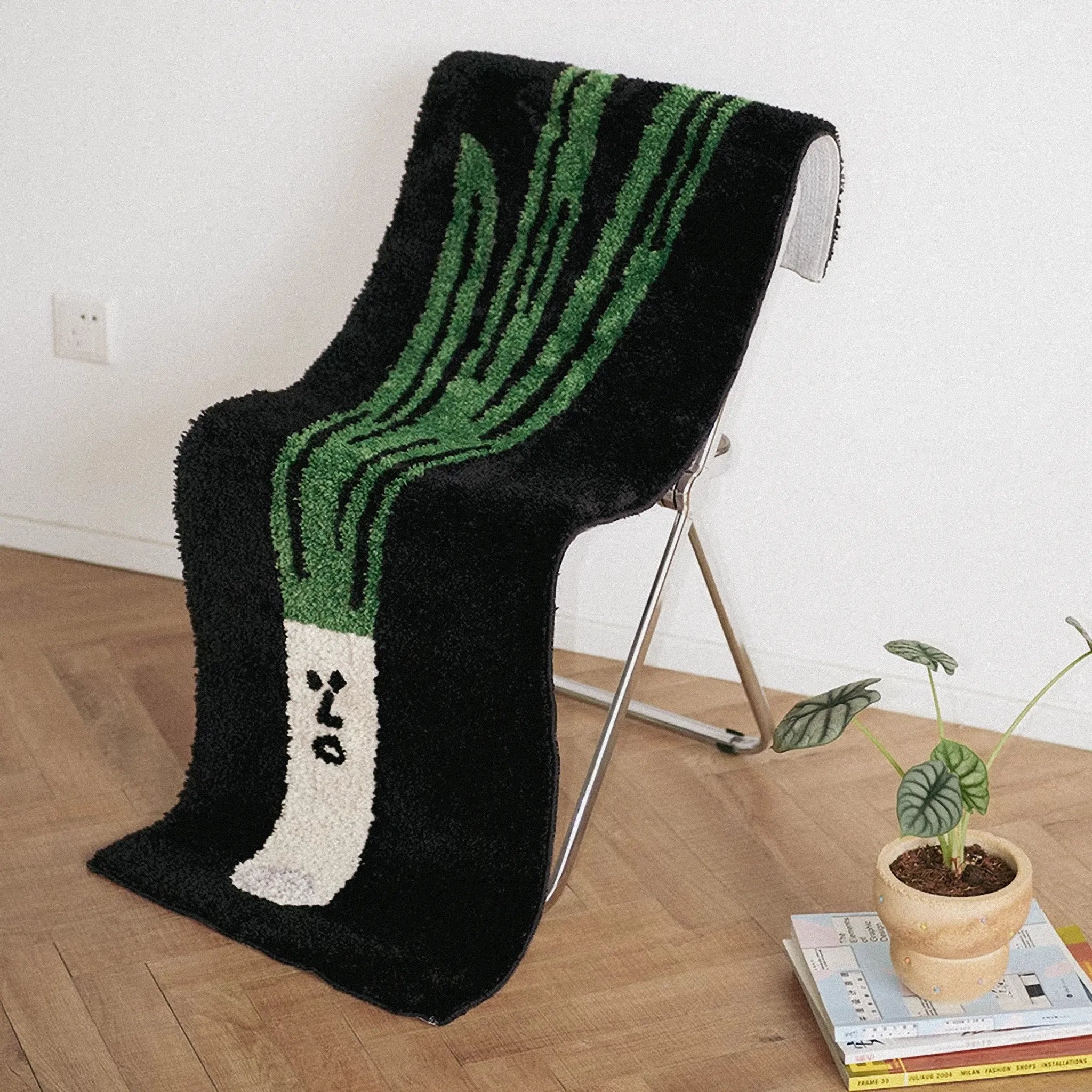 Green Onion Playful Black Runner Rug by Housenfriends on chair with a plant and books on a wooden floor.