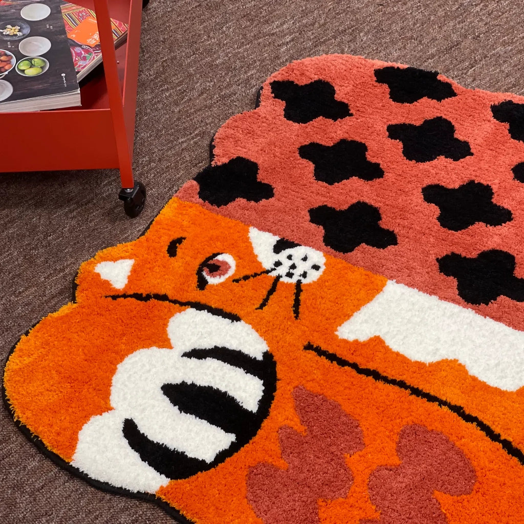 Orange patchwork cat shaped tufted rug on the floor beside a red trolley, showing its playful animal rug outline by Housenfriends