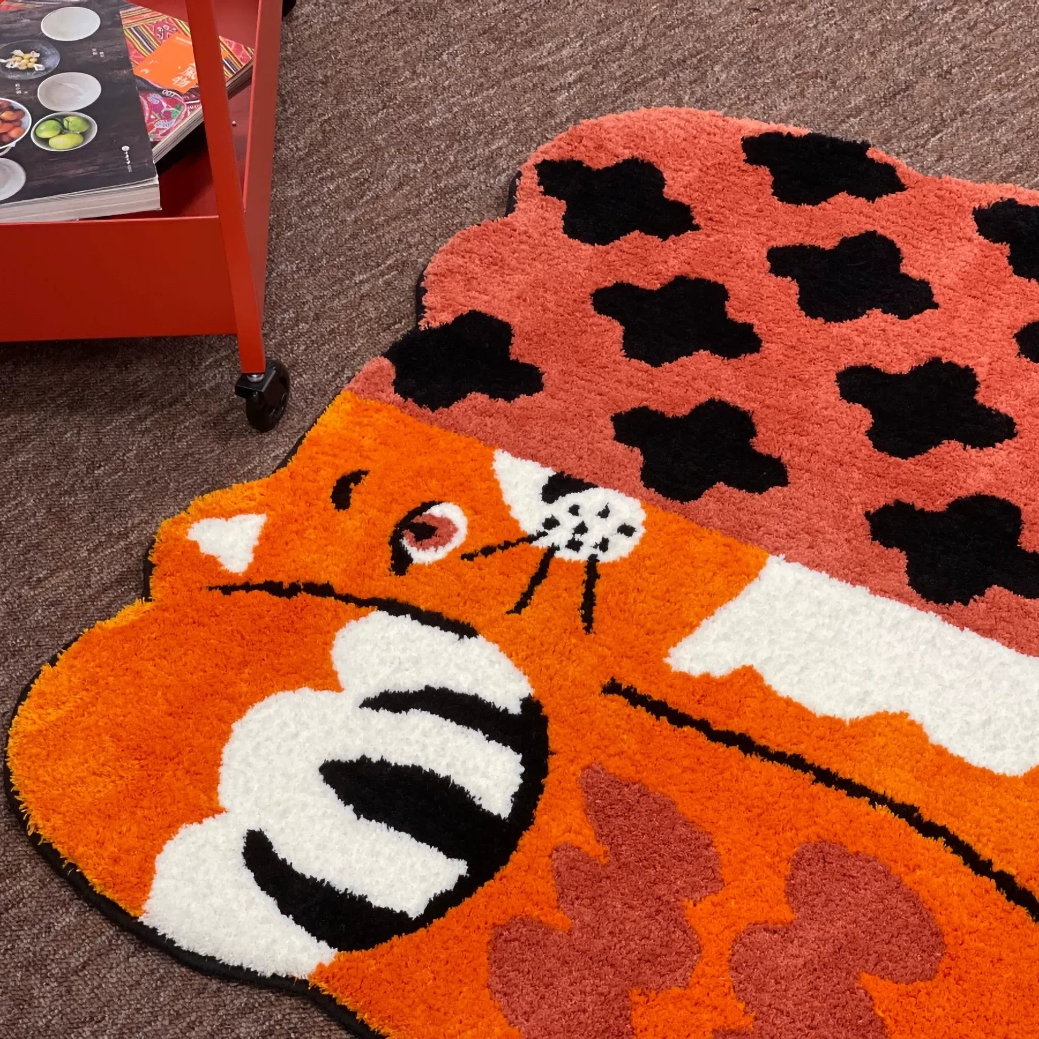 Orange patchwork cat shaped tufted rug on the floor beside a red trolley, showing its playful animal rug outline by Housenfriends