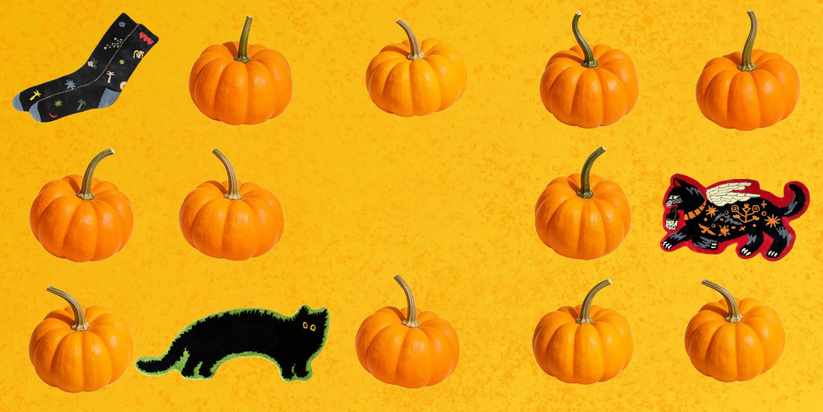 Housenfriends Halloween banner featuring black cat and sock shaped rugs among orange pumpkins on a golden yellow background.