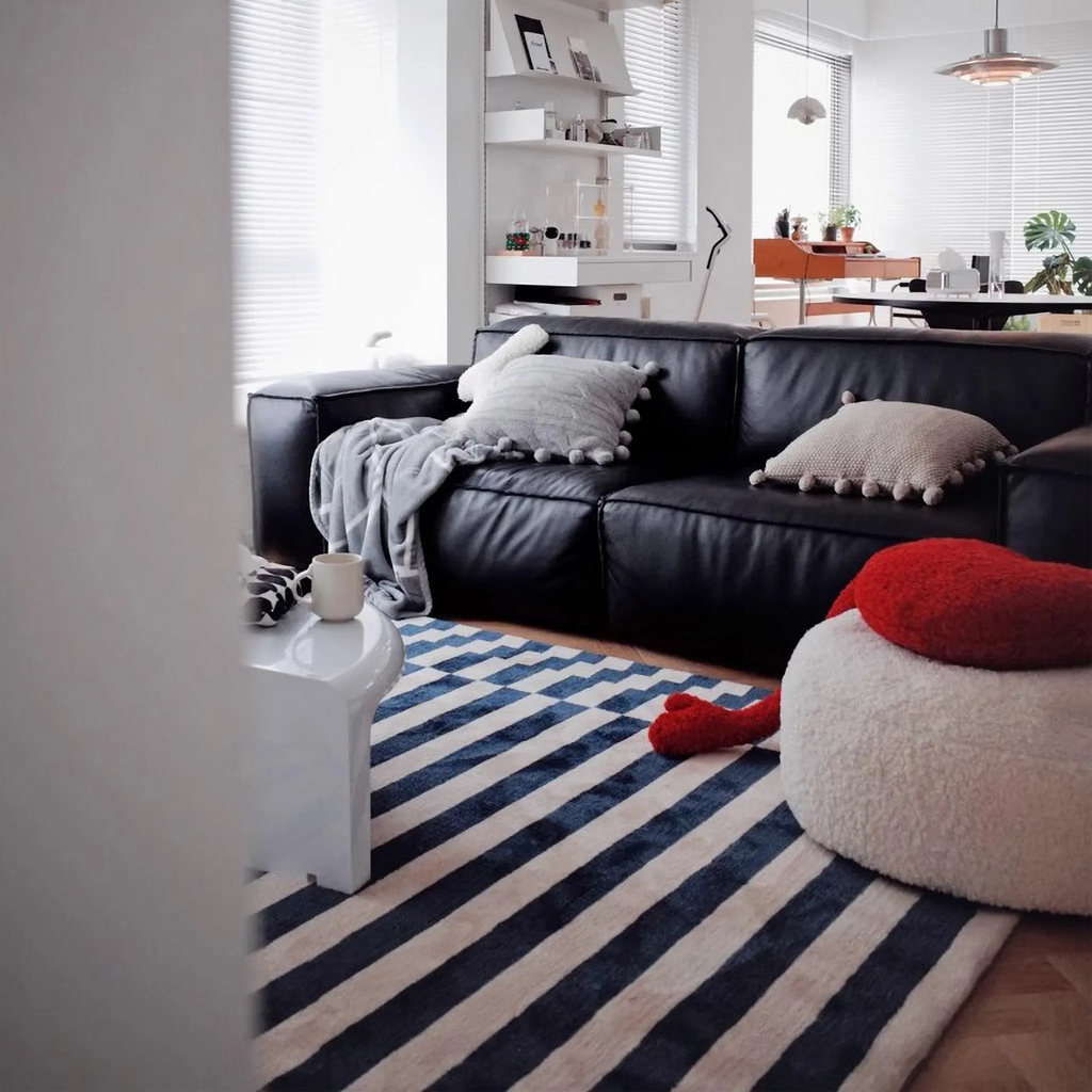Modern living room with a black leather sofa, pillows and Julian Blue & White Offset Striped Modern Rug by Housenfriends.