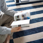 Person sitting on Julian Blue & White Offset Striped Modern Rug reading a magazine