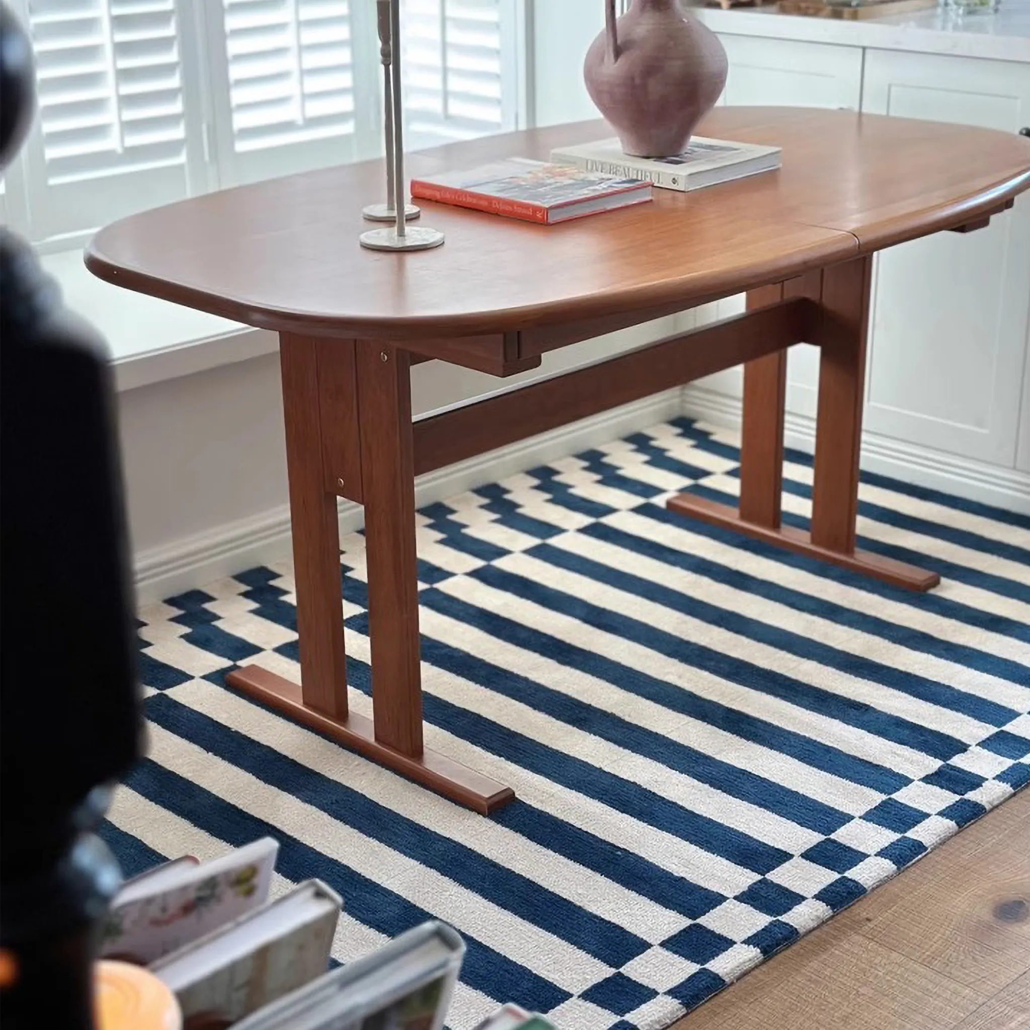 Wooden dining table with books and a vase on Julian Blue & White Offset Striped Rug by Housenfriends.