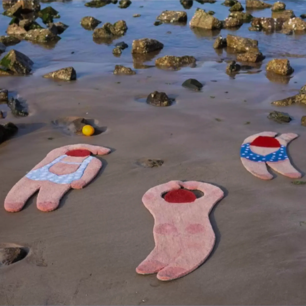 June swimming girl graphic body art rugs by Housenfriends on seaside sand, showing pale blue polka dot, nude curved back and navy swimsuit tufted rug designs