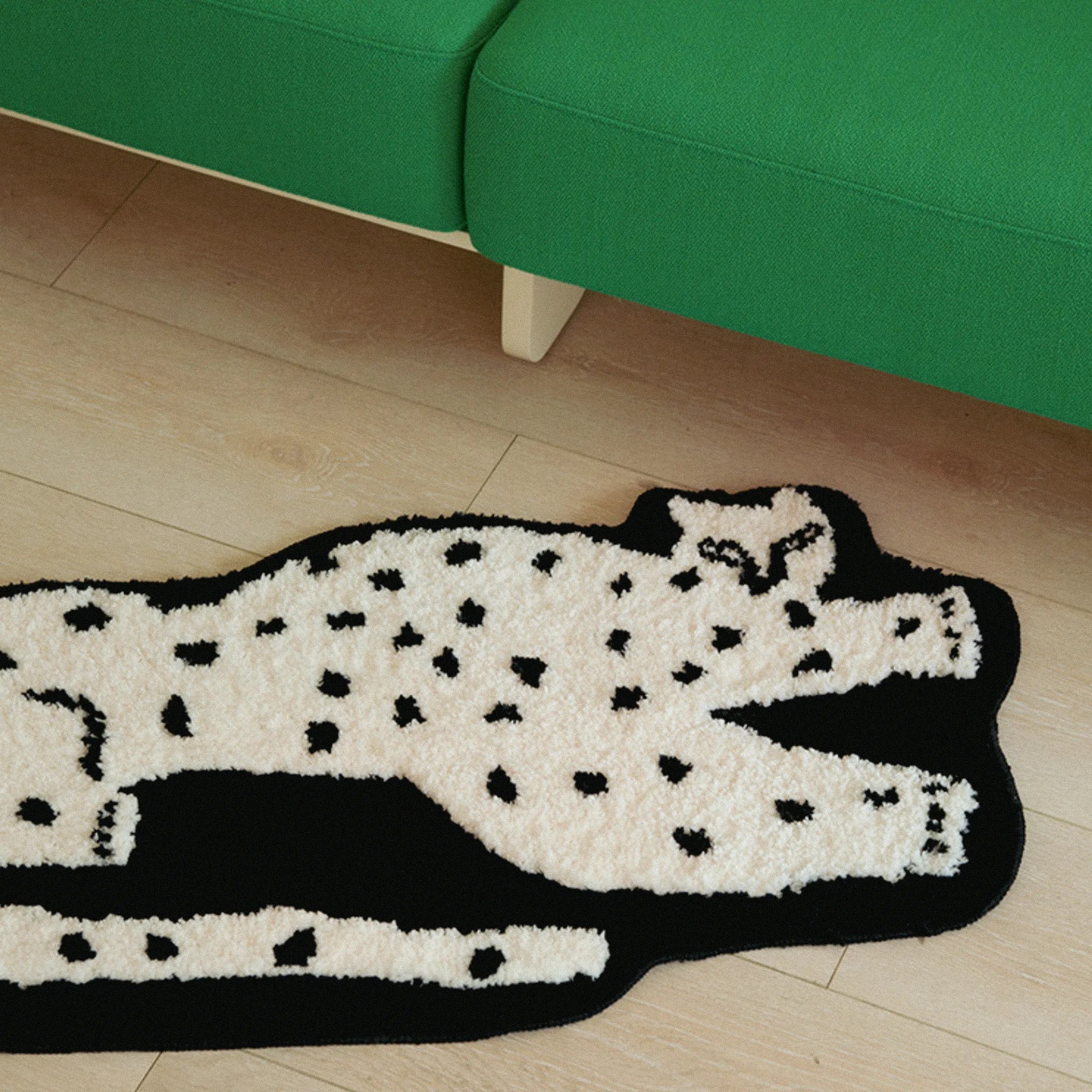 Layla Black Base White Leopard Shaped Tufted Rug on a wooden floor with a green couch.