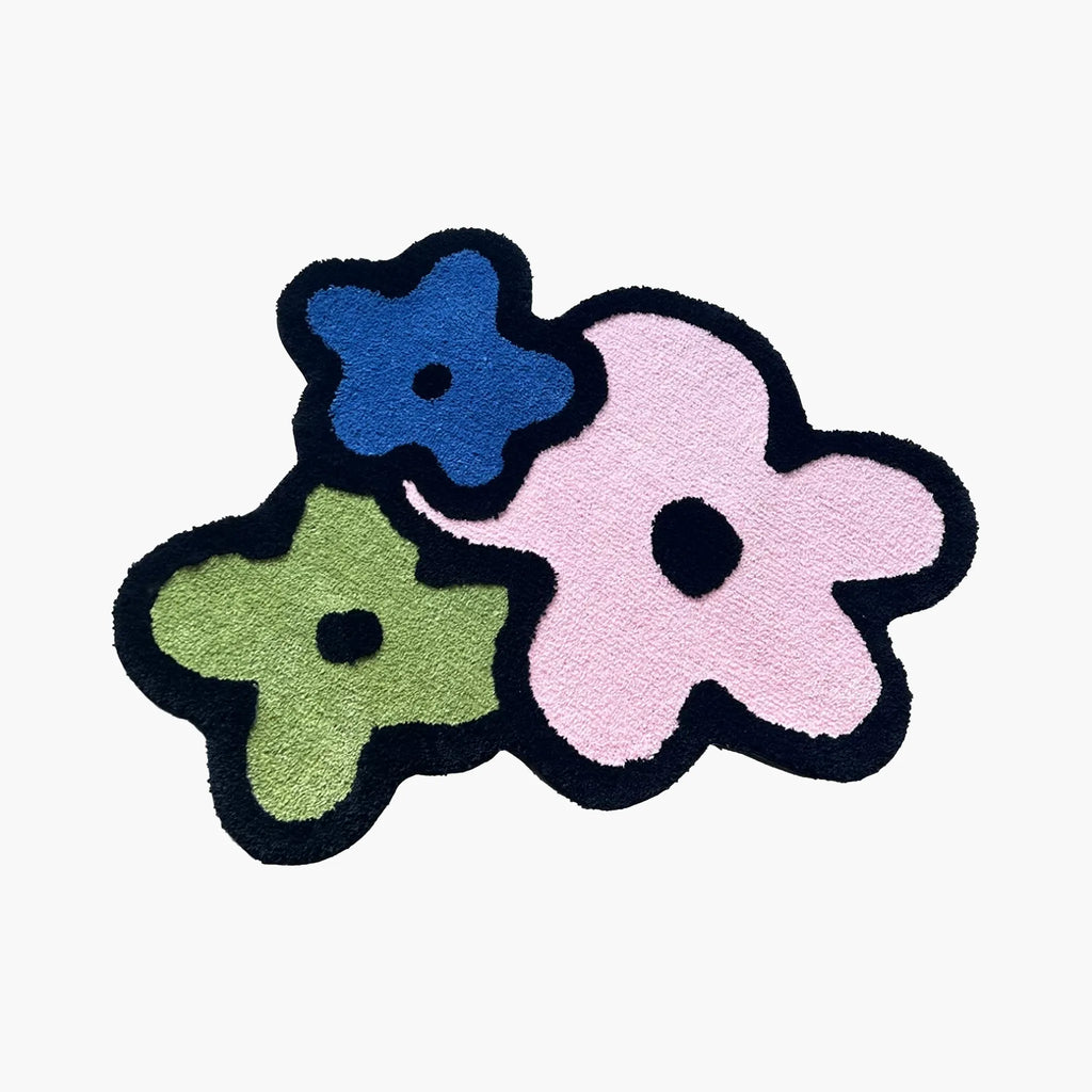Lola Pastel Pink Blue Green Graphic Flower Shaped Tufted Rug by Housenfriends on white background, pastel flower shaped rug with black outline, pink blue green petals and playful retro mood