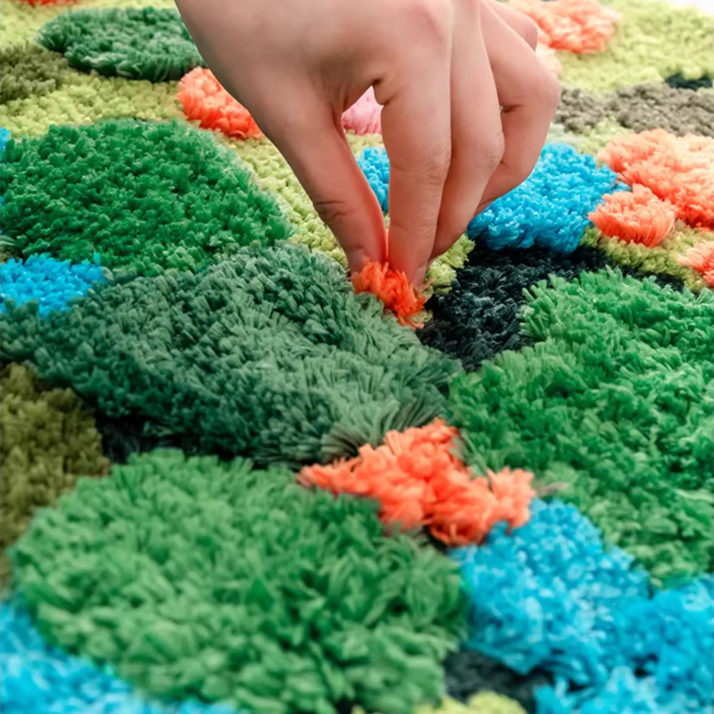Close-up of Merryn Green Moss Garden High Low Tufted Rug by Housenfriends, showing raised mossy texture and colourful wildflower tufts under hand.