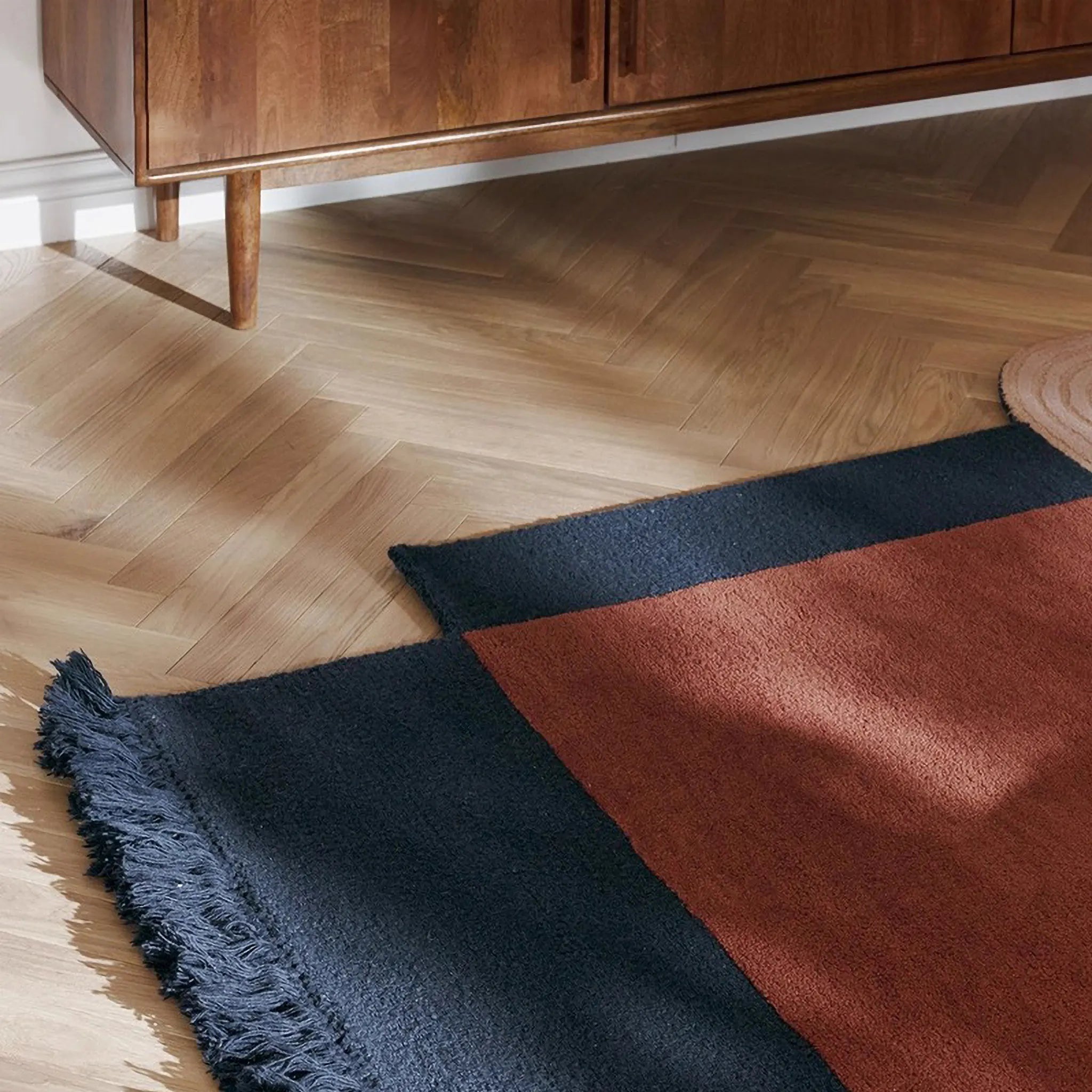 Mira Rust Mustard Navy Beige Abstract Irregular Fringe Wool Rug on a wooden floor with a wooden cabinet in the background.