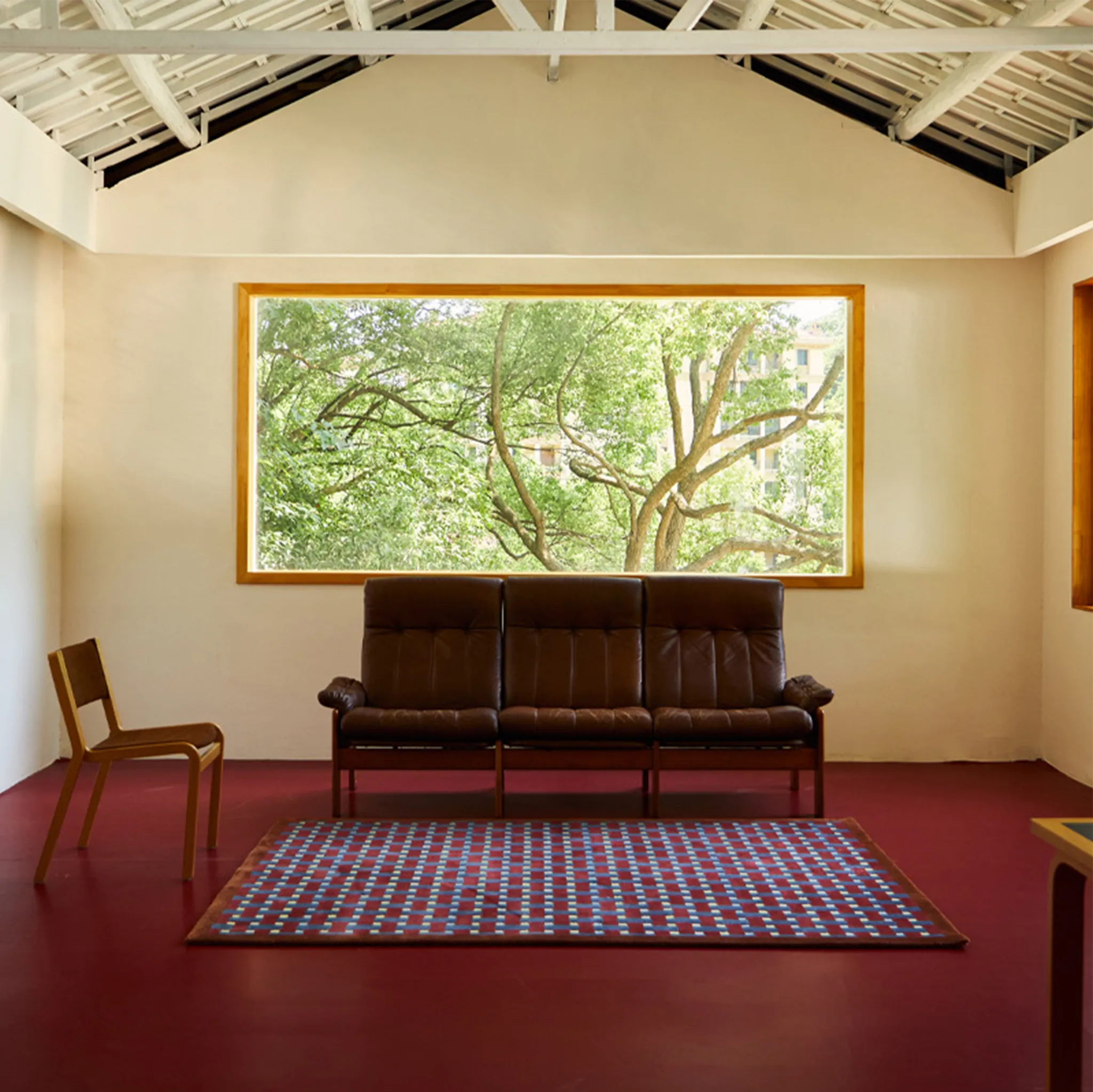 Living room with a brown leather sofa on Mondrian Red Navy Beige Retro Checkered Wool Rug, a chair, and window showing greenery.