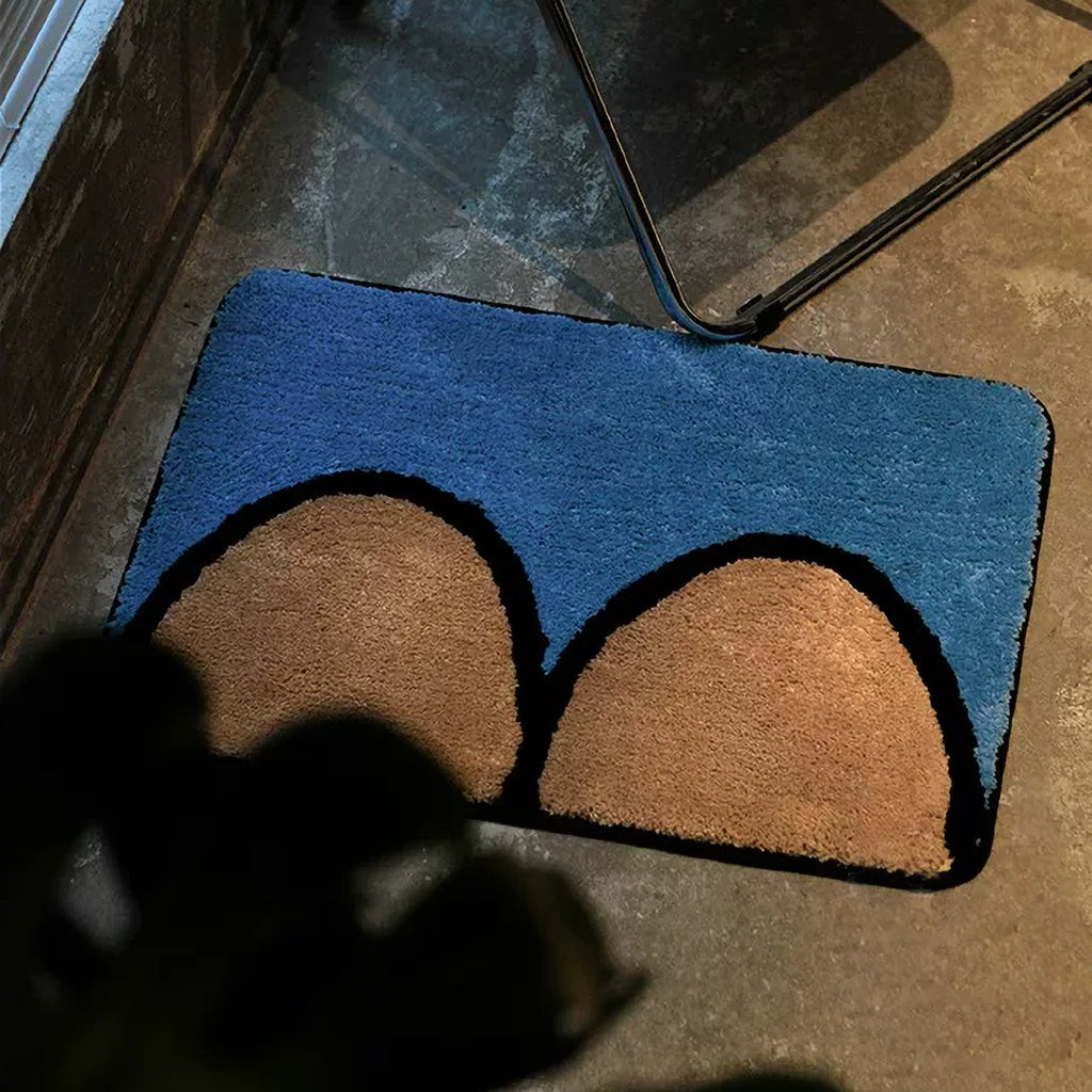 Nico Blue & Tan graphic abstract breast body art tufted rug on a dark floor beside a chair, Housenfriends