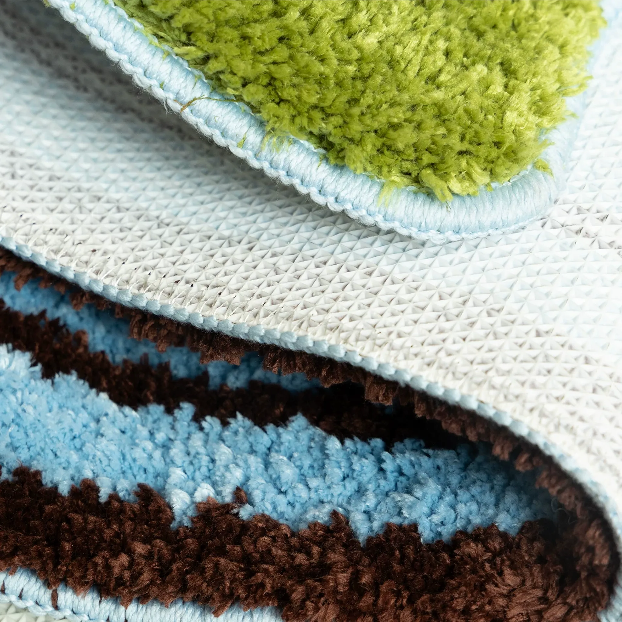 Detail of pastel blue and green sock shaped tufted rug with soft pile texture, stitched edge and non-slip backing by Housenfriends