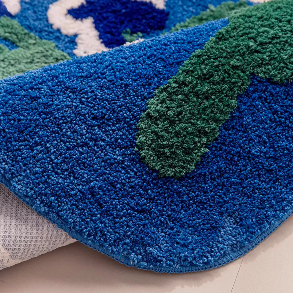 Close-up corner of Orla blue floral rug showing high-low tufted texture and moss green detail on an organic shaped edge