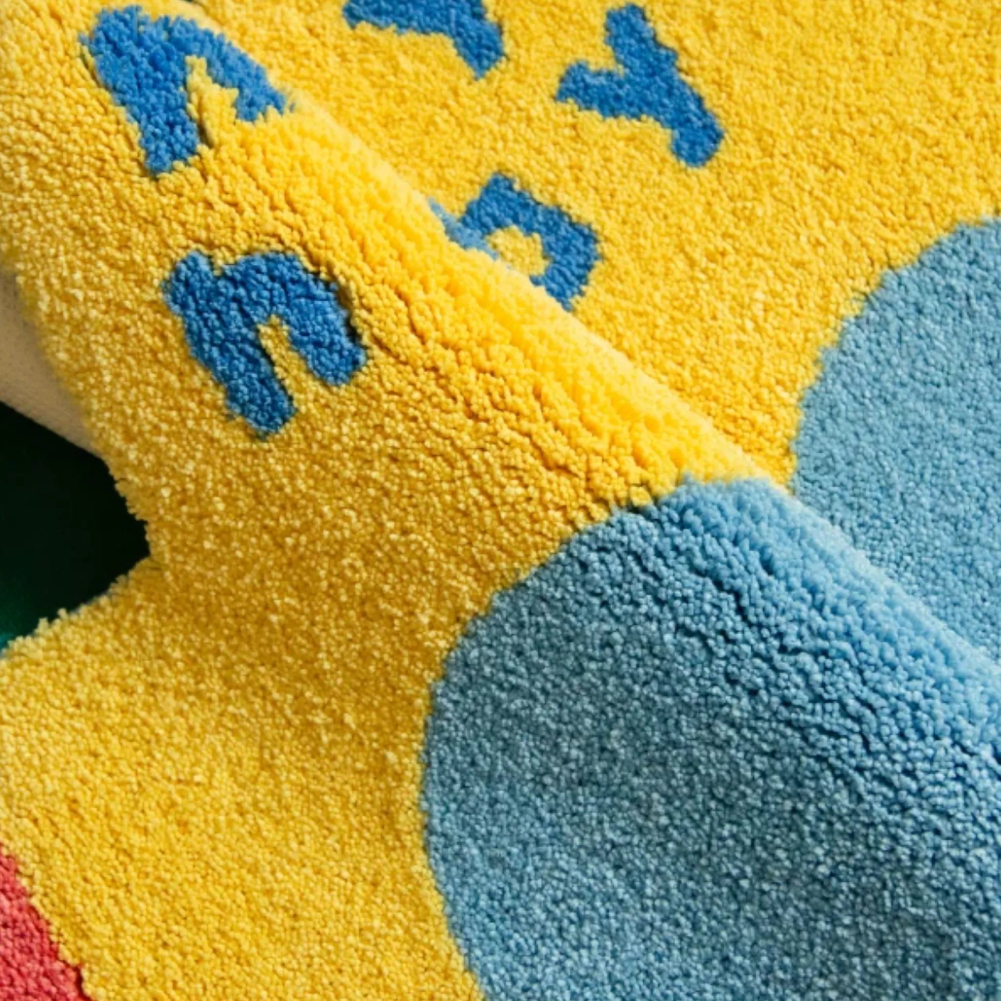 Pip Yellow & Blue Happy Holiday Graphic Car Shaped Tufted Rug by Housenfriends close up, shaggy graphic car rug with yellow pile, blue lettering and soft tufted texture