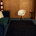 Modern living room with a green sofa, white chair, and Pure Black Minimalist Modern High Low Hand Tufted Rug by Housenfriends.