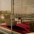 Modern outdoor seating area with a sofa, table, and the Burgundy Diamond Modern High Low Tufted Rug on a patio with glass walls.
