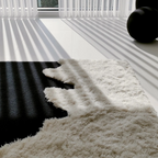 Close-up of a fluffy Reynisfjara Black Shore White Waves rug with shadows on a floor.