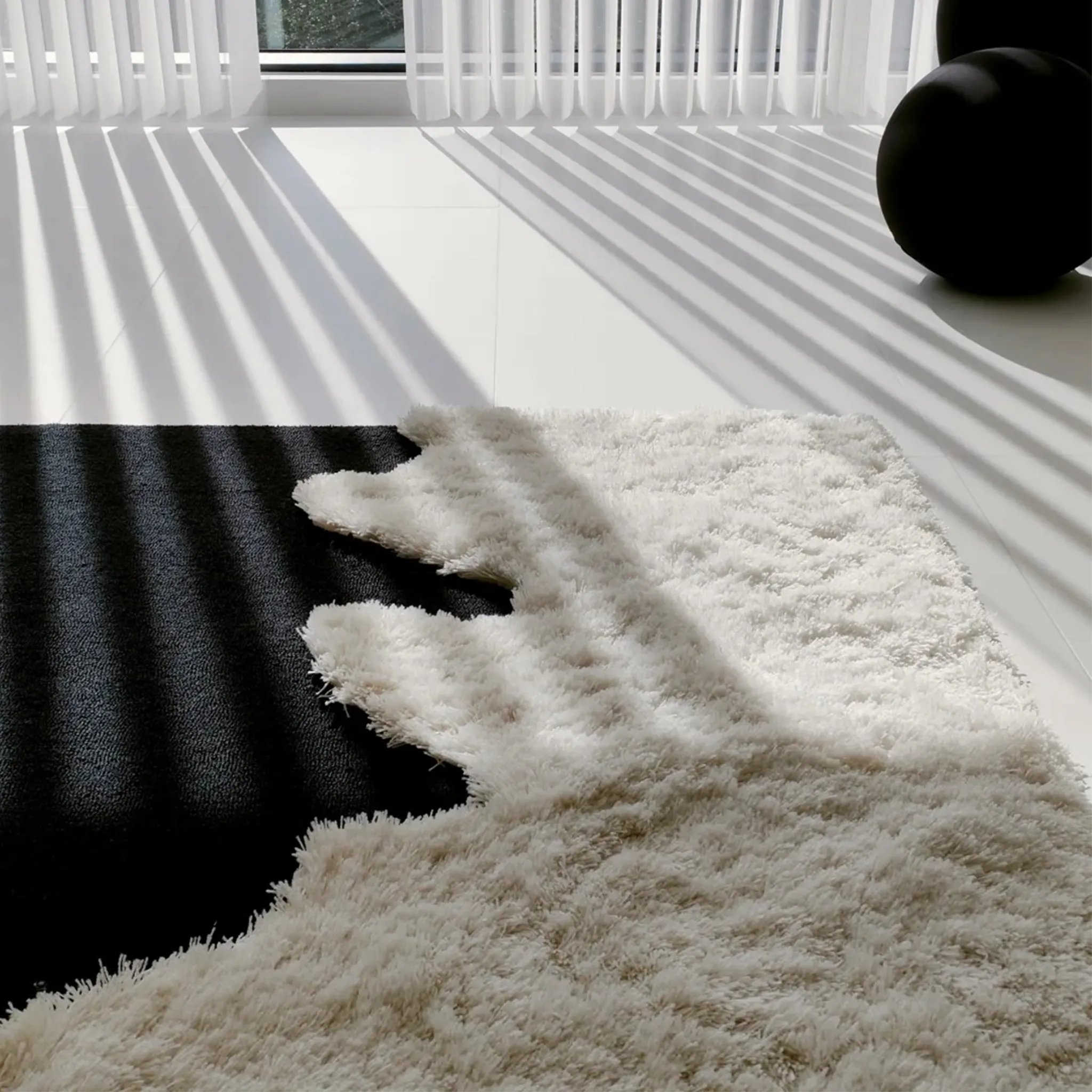 Close-up of a fluffy Reynisfjara Black Shore White Waves rug with shadows on a floor.