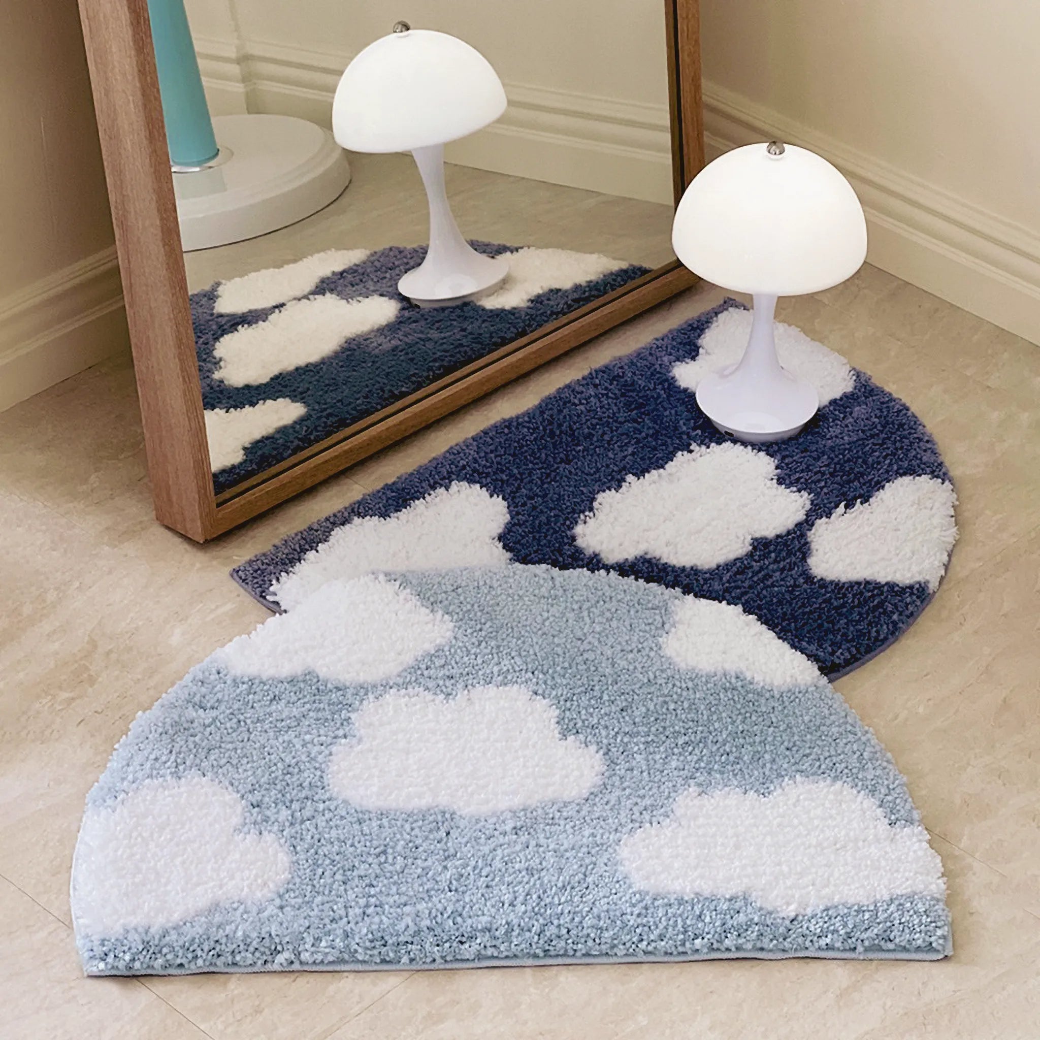 Two cloud-patterned rugs by Housenfriends on a beige floor with a mirror reflecting a white lamp.