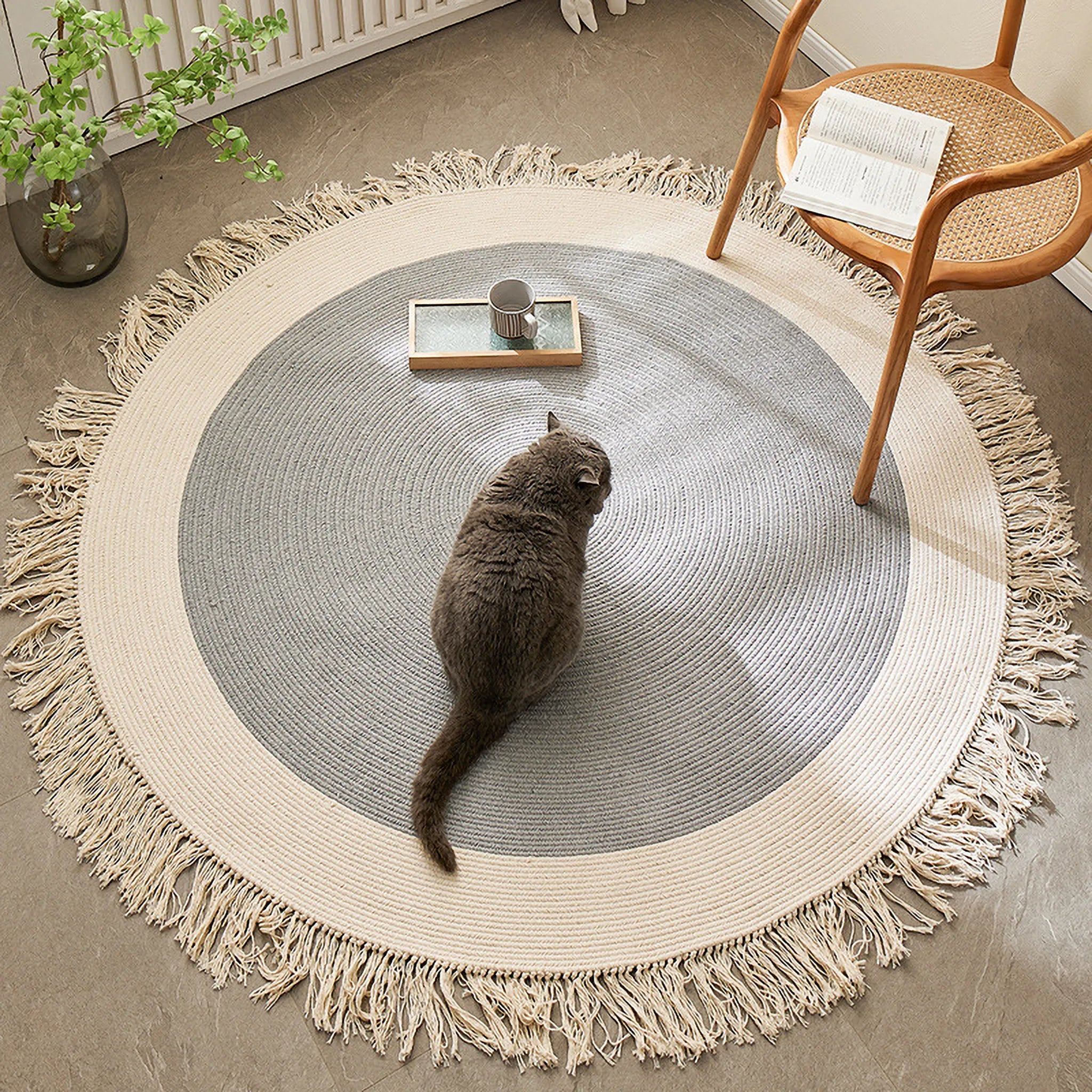 Signe grey and natural fringed round hand-braided cotton blend rug in a cosy room corner with chair and cat by Housenfriends