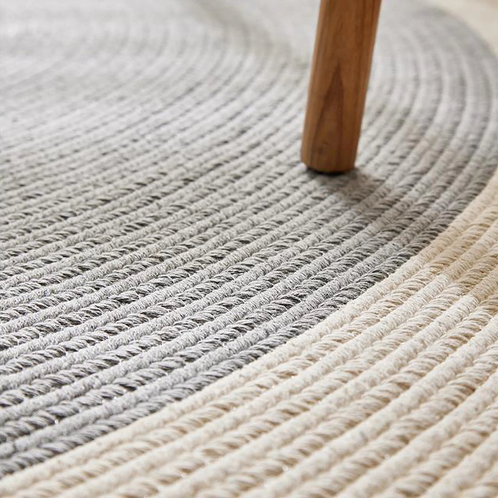 Signe grey and natural fringed round hand-braided cotton blend rug close-up with chair leg for scale by Housenfriends