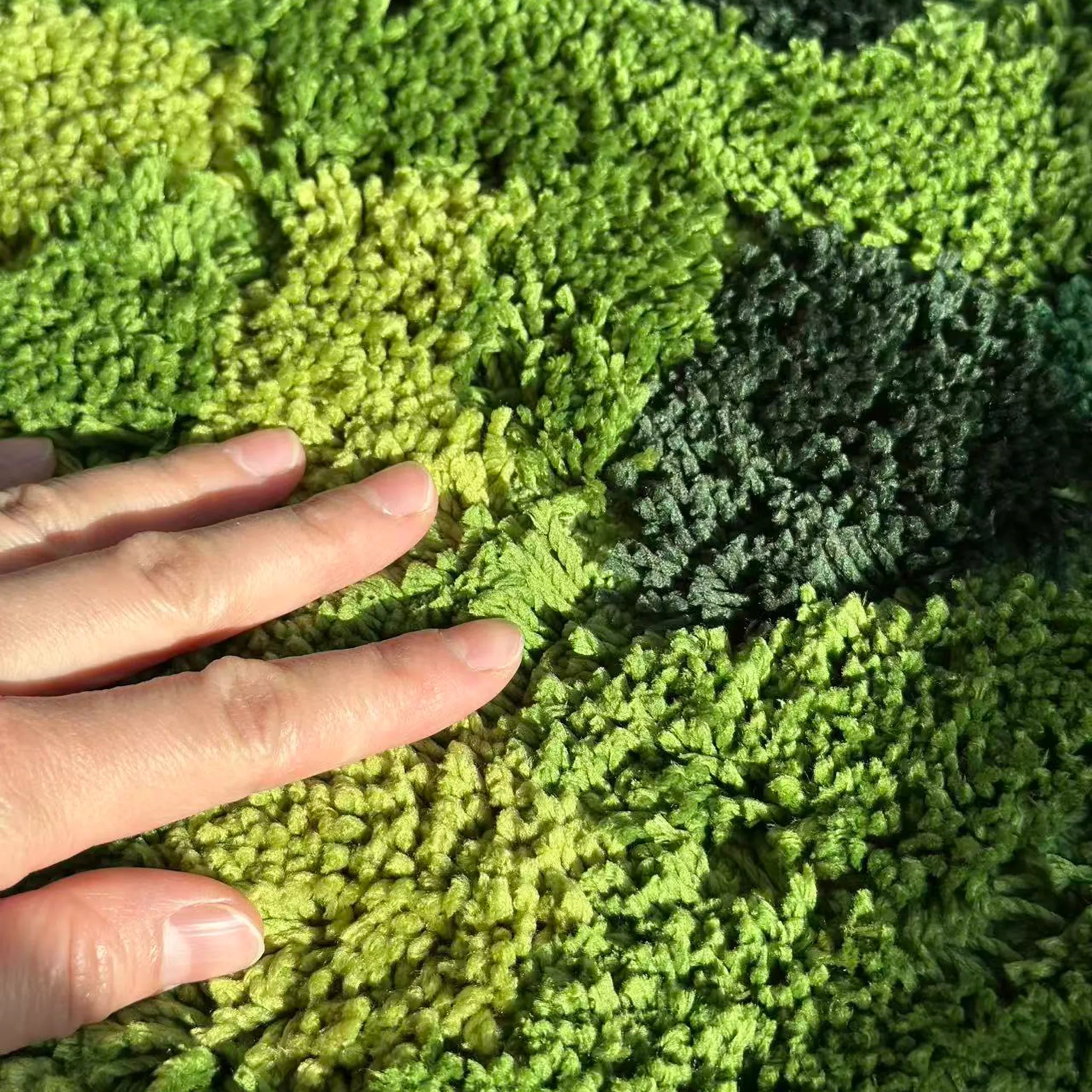 Hand touching Sylvie moss green tufted high-low texture, showing organic forest tones by Housenfriends