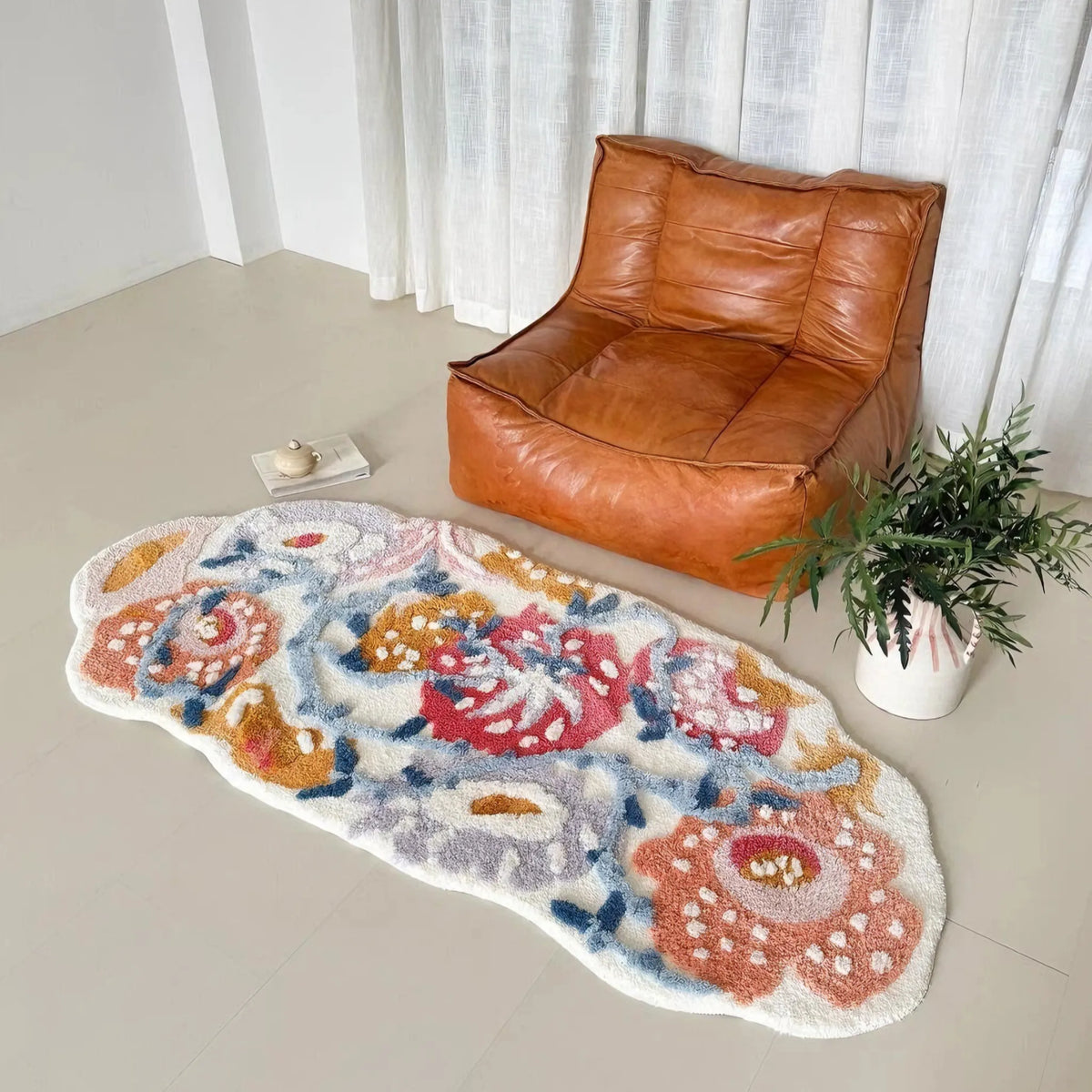 Celia colourful floral tufted runner rug with pink, orange and blue flowers on a cream background, beside a brown leather lounge chair and potted plant.