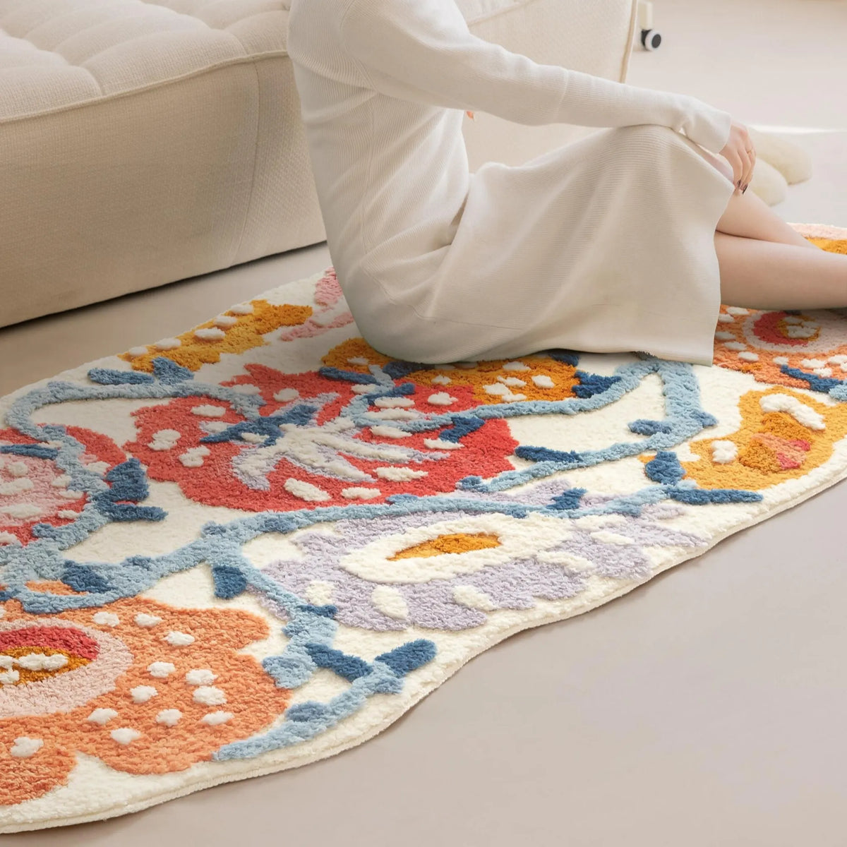 Person sitting on the Celia colourful floral tufted runner rug beside a cream sofa, showing its raised flower patterns and irregular edges.