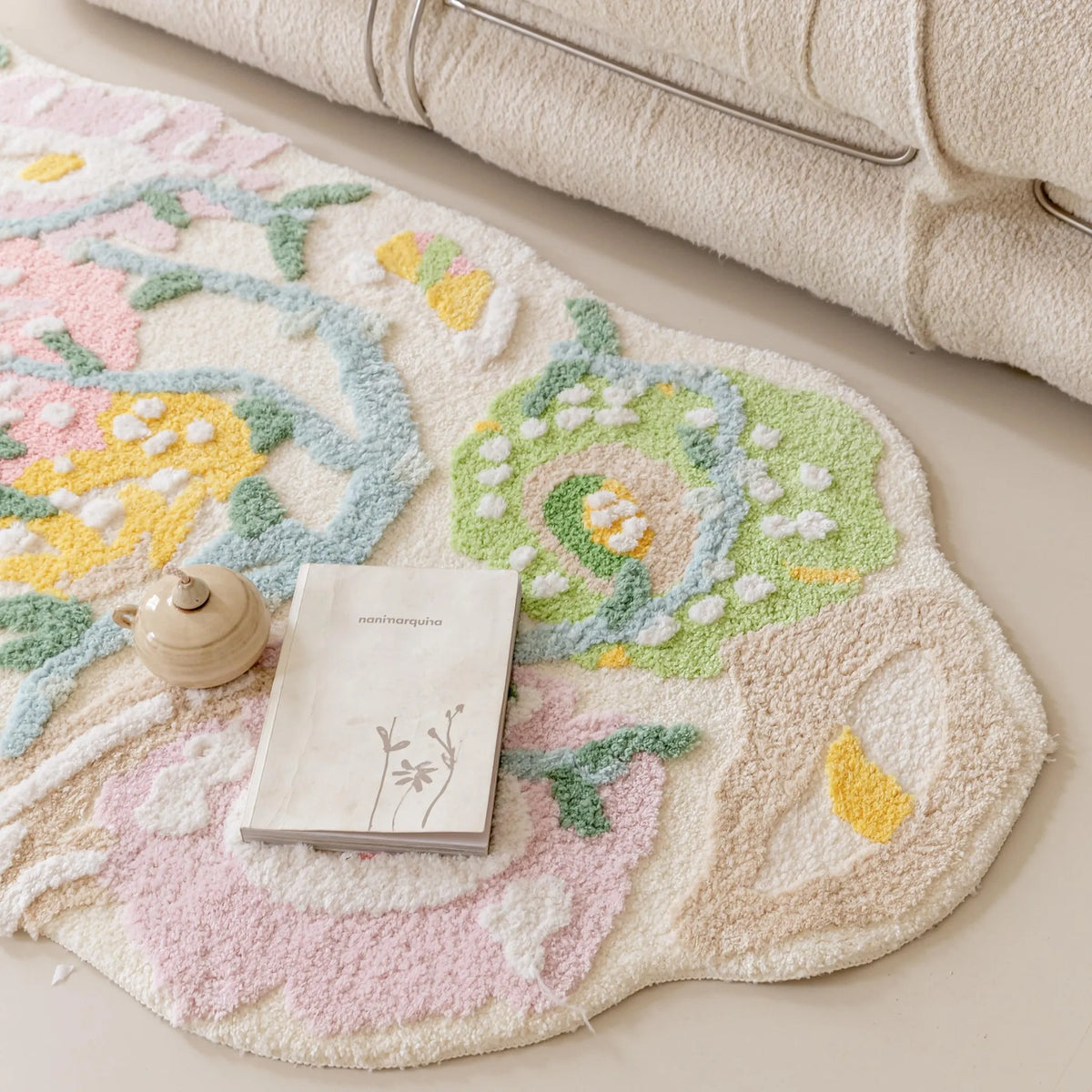 Close-up of the Housenfriends Celia pastel floral irregular runner rug with an open book and a small beige ceramic teapot resting on its raised pink, green and yellow floral pattern.