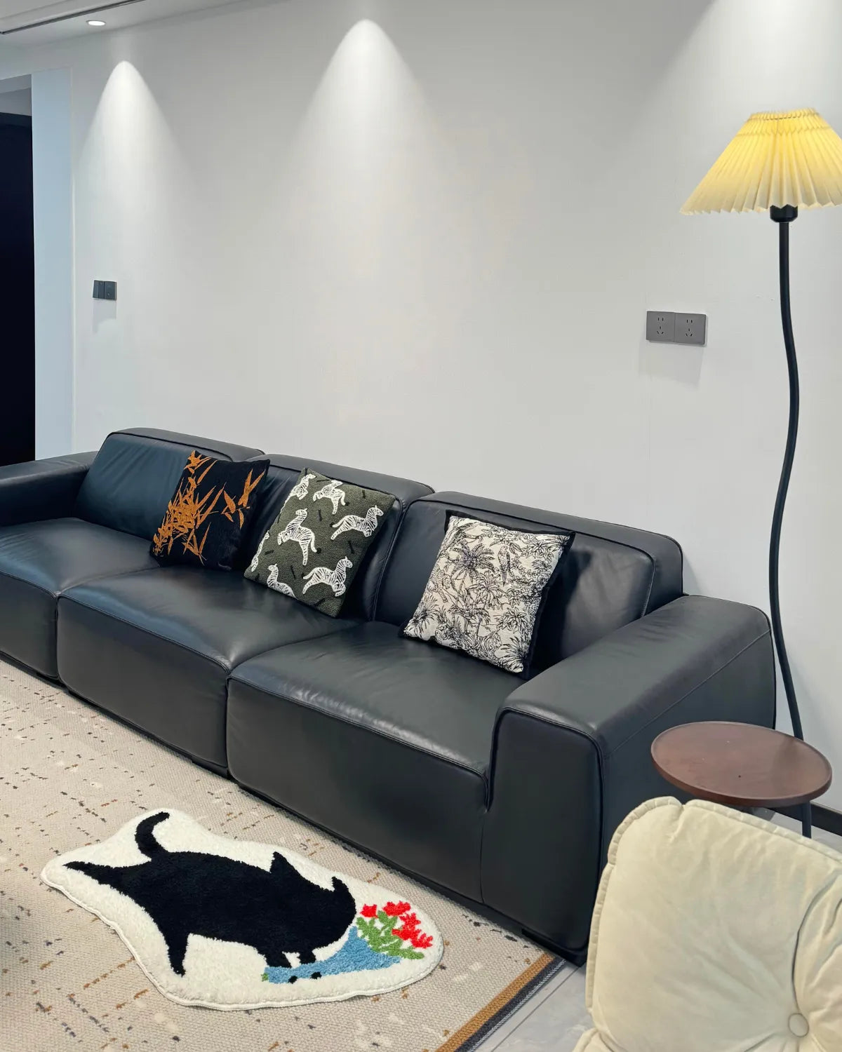 Housenfriends floral black cat tufted rug in a contemporary living room, layered in front of a black leather sofa.