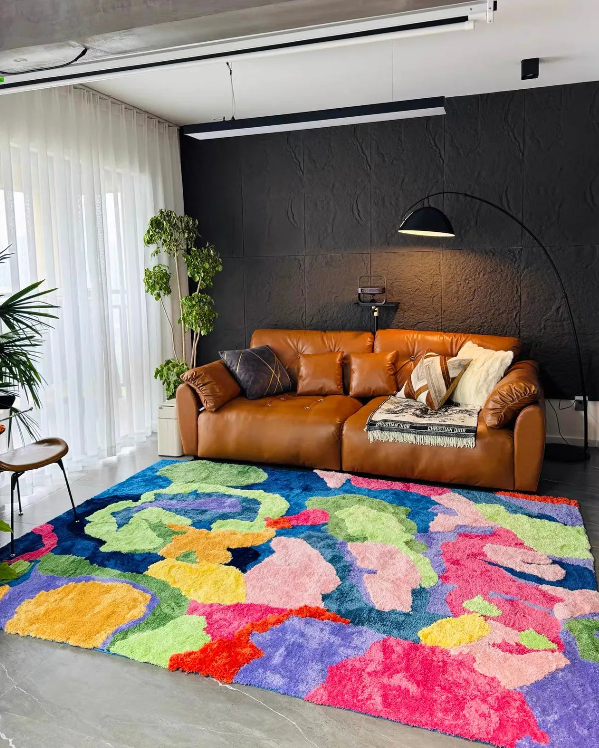 Housenfriends Freya multicoloured abstract floral high-low tufted rug in a dark living room, in front of a caramel leather sofa.