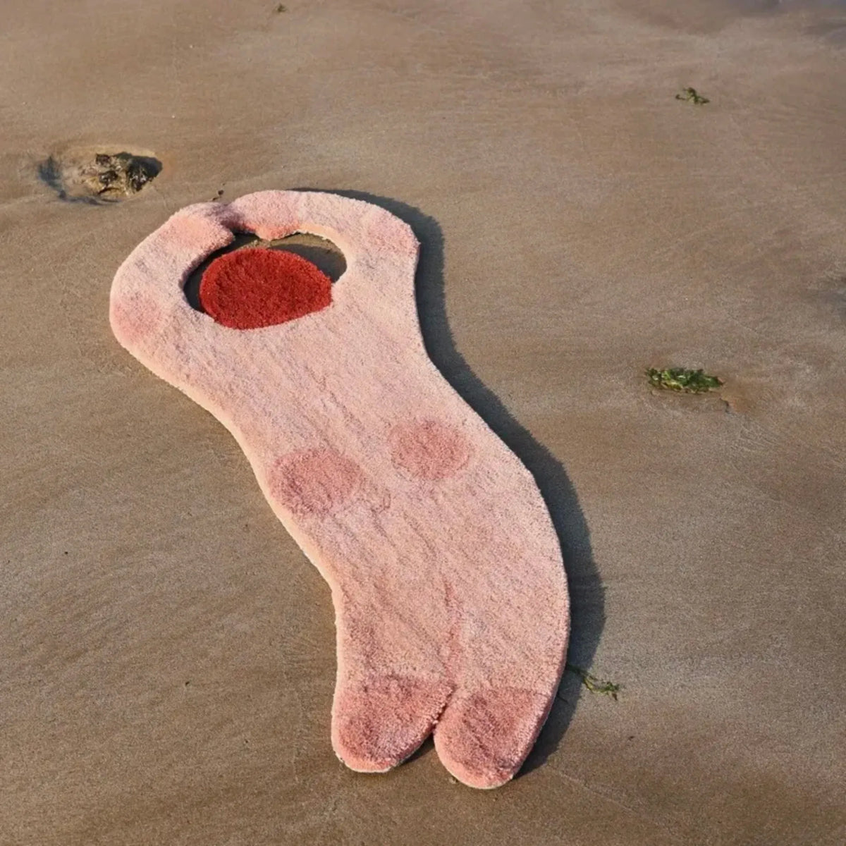 June Nude Pink Swimming Girl Body Art Tufted Rug by Housenfriends, showing a curved figure with arms raised overhead, red-brown hair and soft pink body markings on a sandy beach.